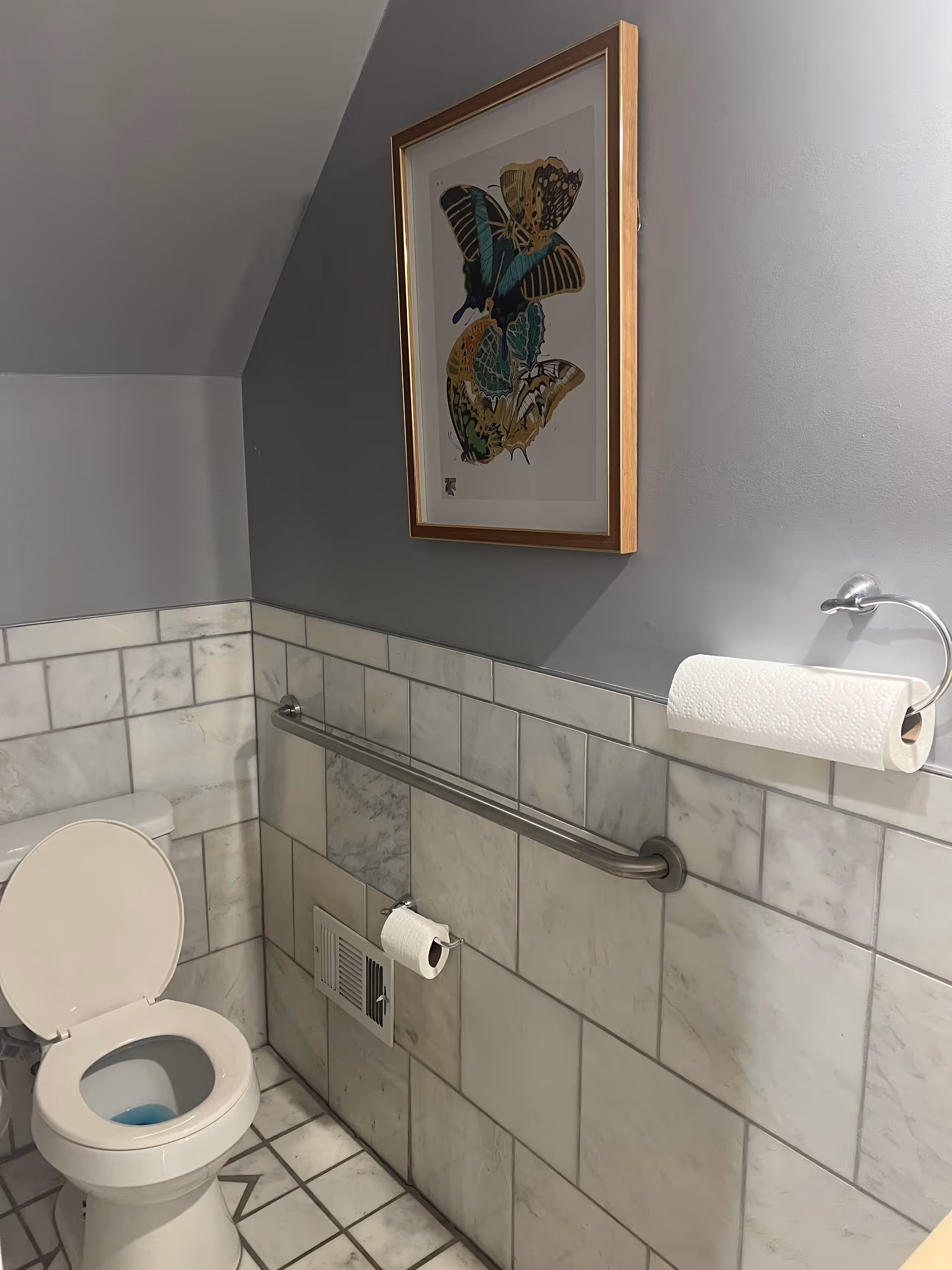 Grey bathroom with tiled walls, toilet, and butterfly artwork.