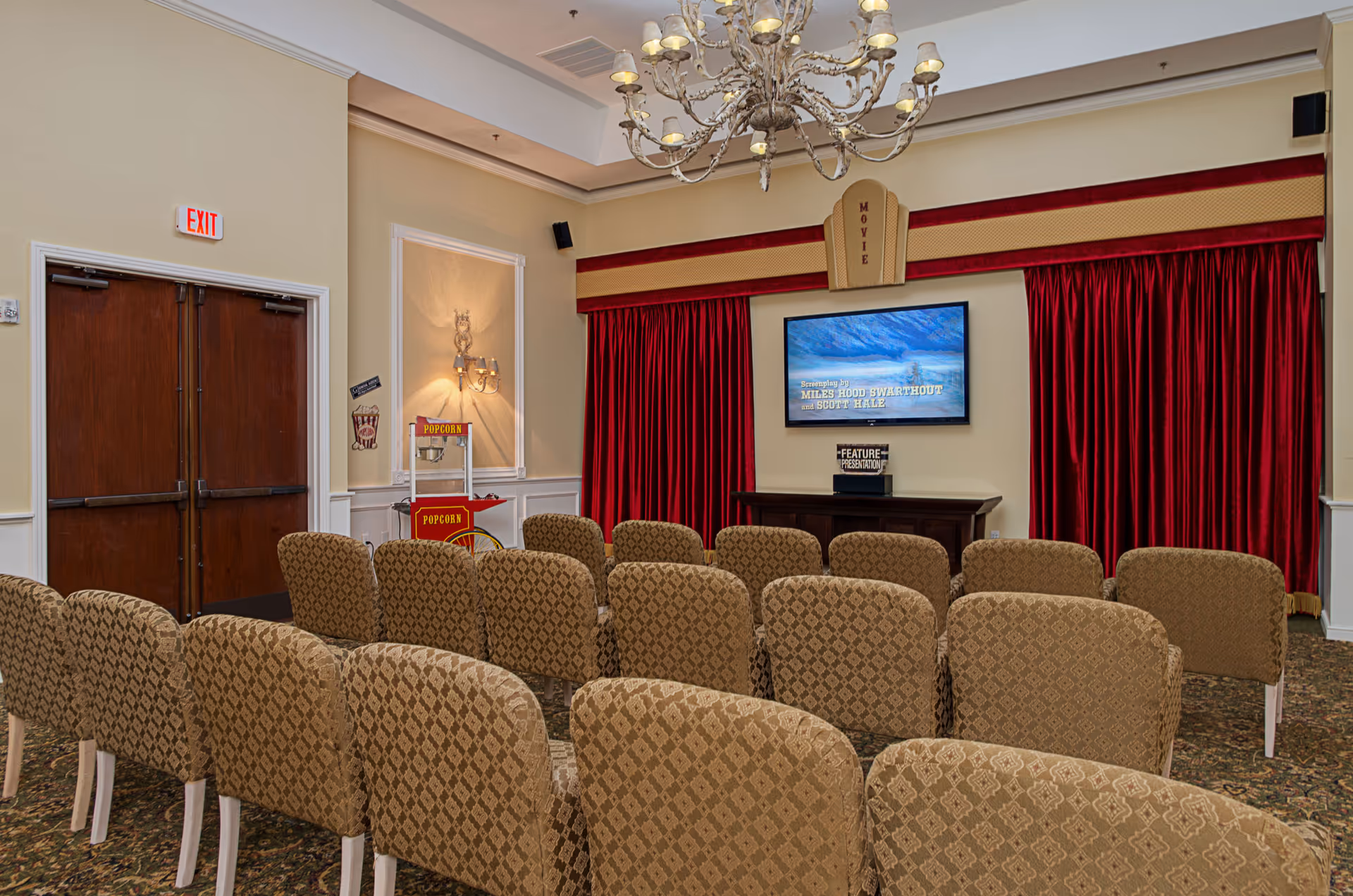 A senior living facility theater with rows of upholstered chairs, red curtains, and a screen.