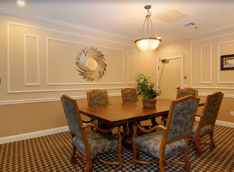 Well-lit dining room with a wooden table, eight upholstered chairs, and decorative wall panels.