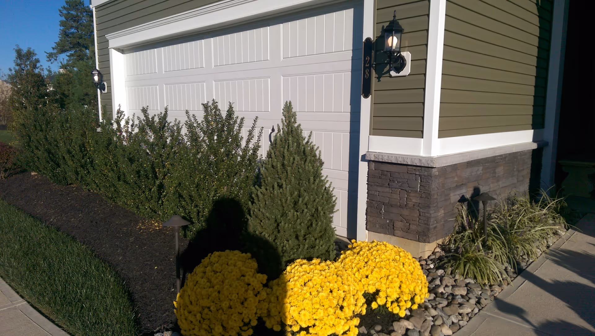Exterior view of a senior living facility entrance with beige siding, stone accents, and yellow flowers.