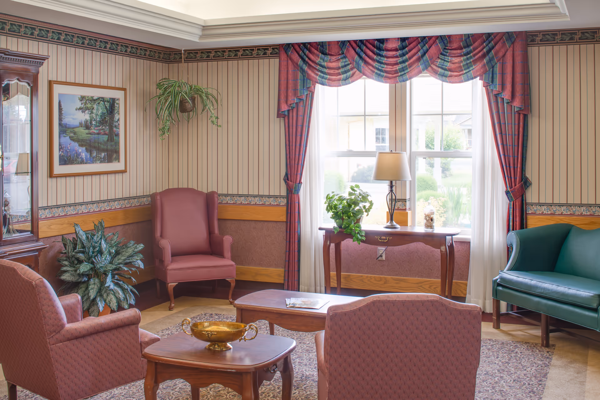 Cozy senior living lounge with pink chairs, a green sofa, plants, and a large window.