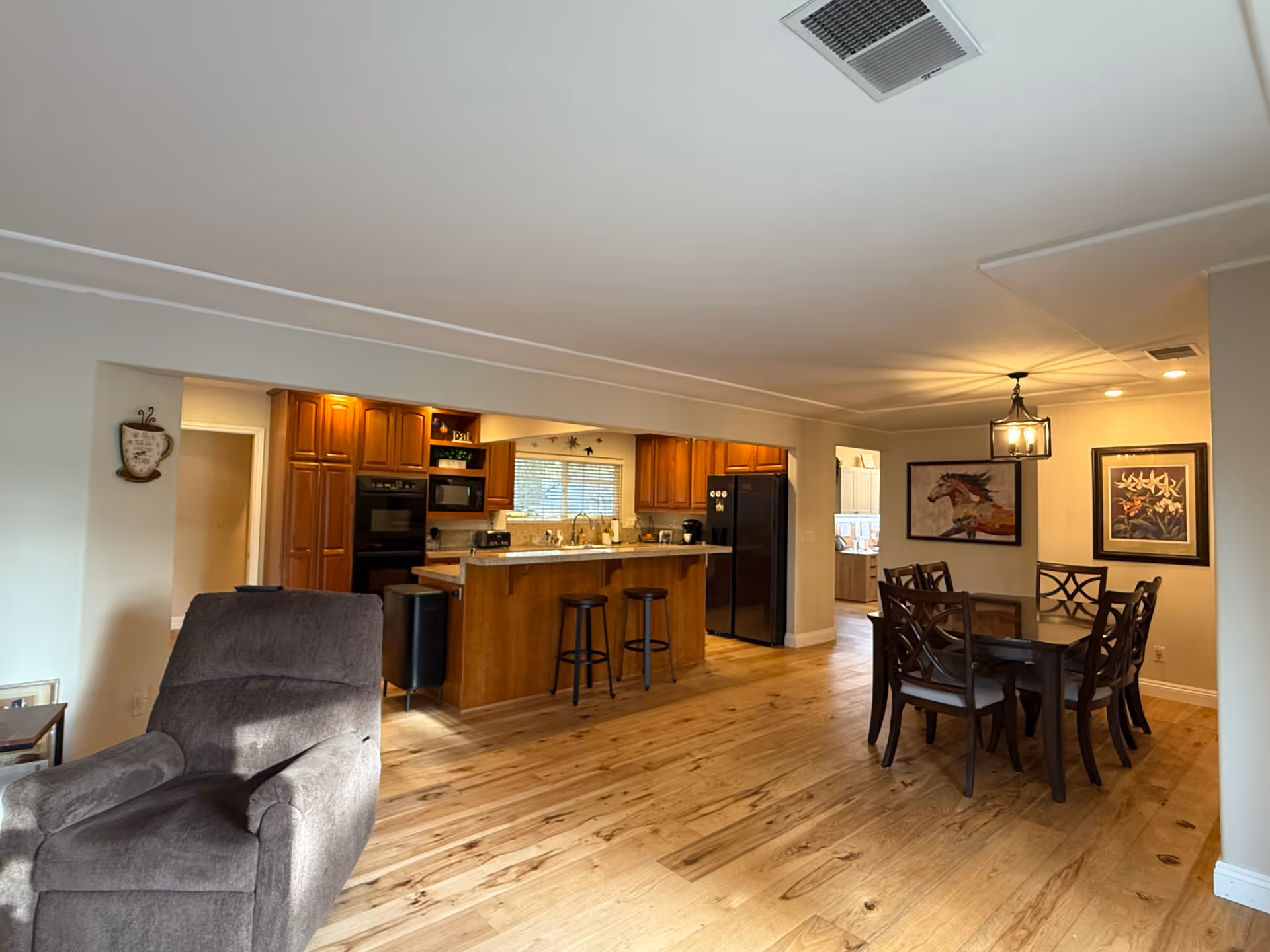 Open-concept living area with kitchen island, stools, dining table, and warm wooden floors.