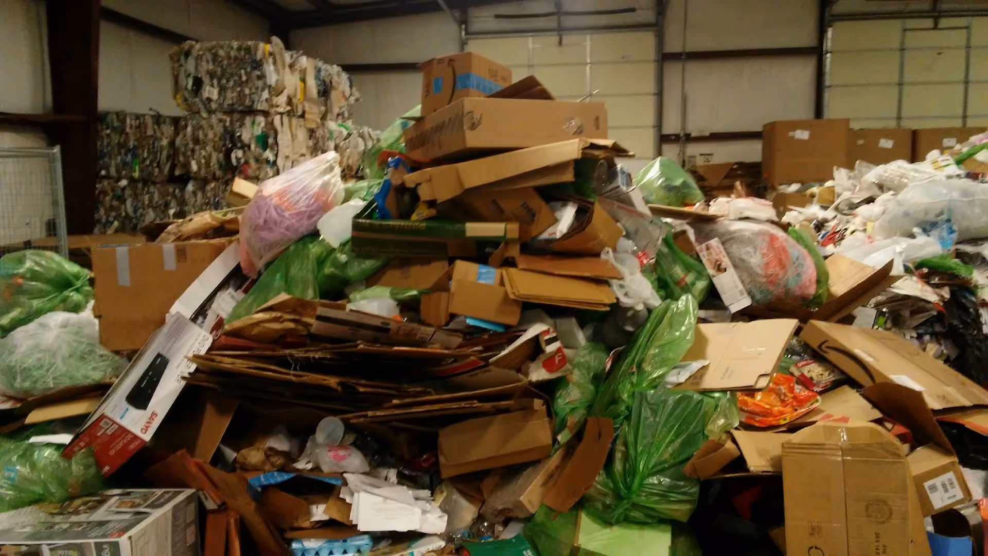 Interior warehouse filled with piled cardboard, boxes, and bags of recycling materials.