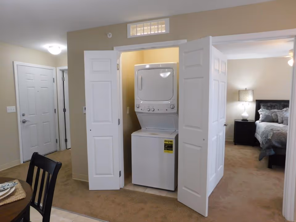 Open laundry closet with stacked washer and dryer beside a bedroom in a residential suite.
