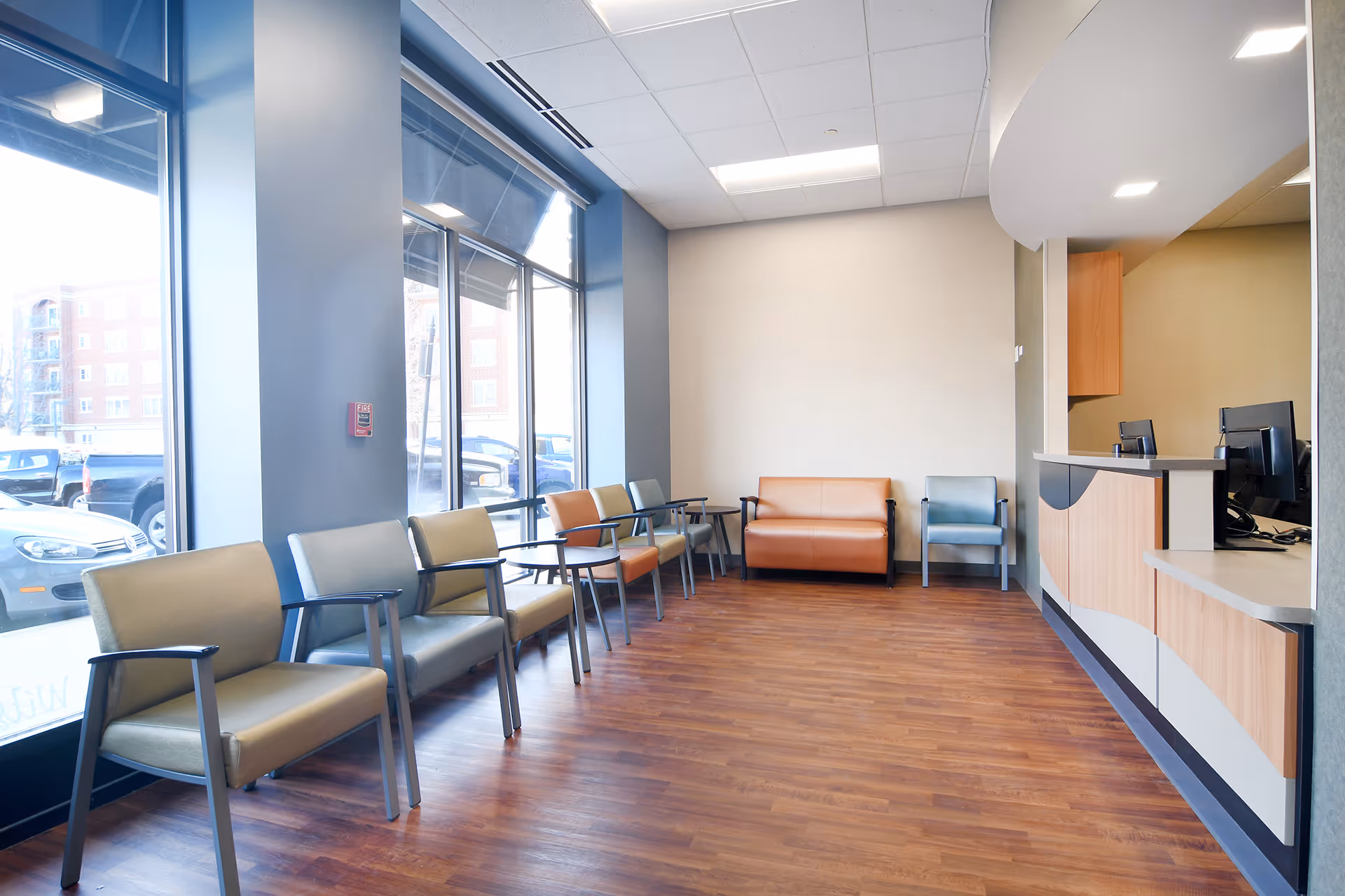 A bright waiting lobby with row of chairs, a curved reception desk, and wood floors.