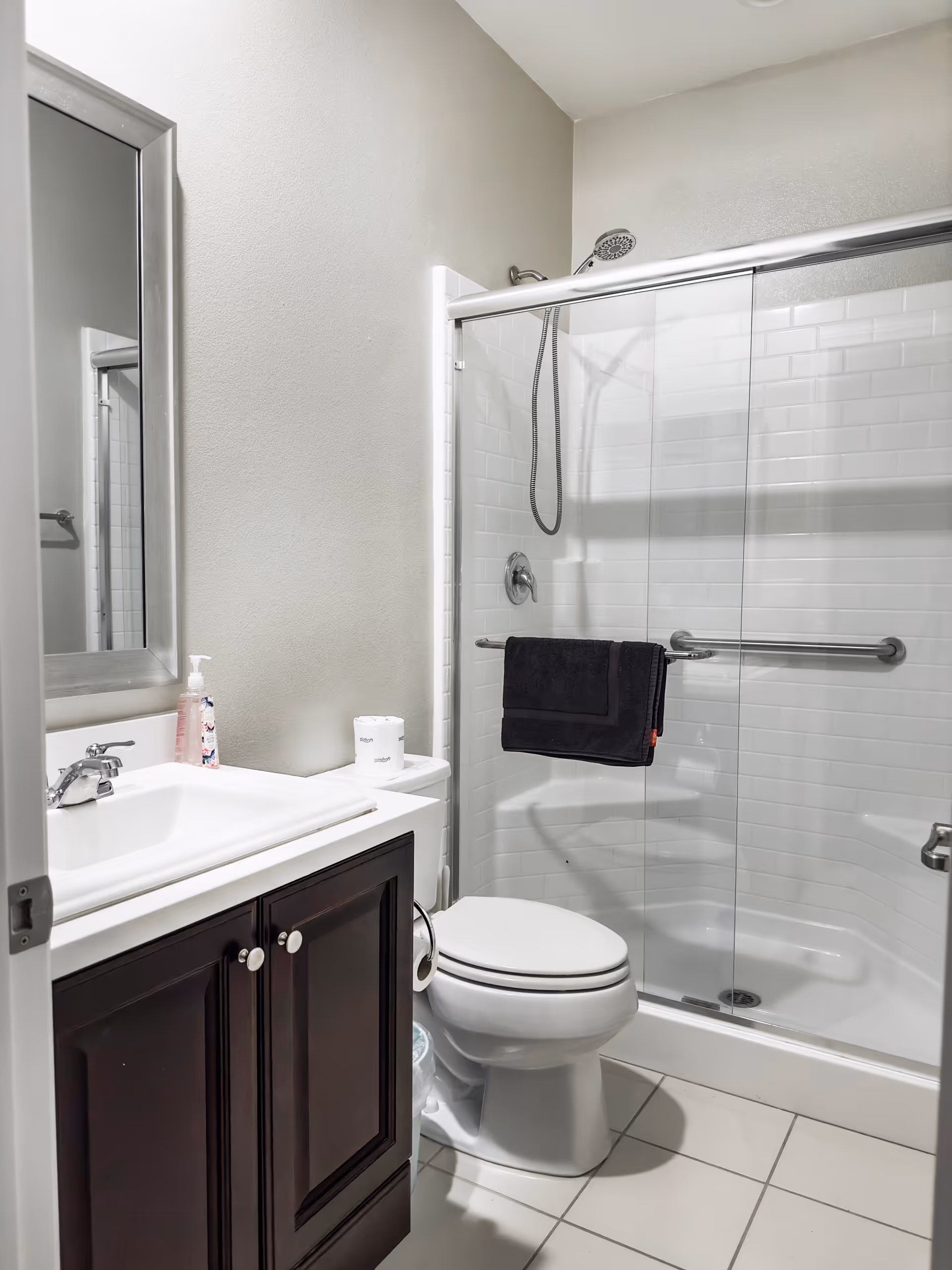 Compact bathroom with sink, mirror, toilet, and glass-shower enclosure.