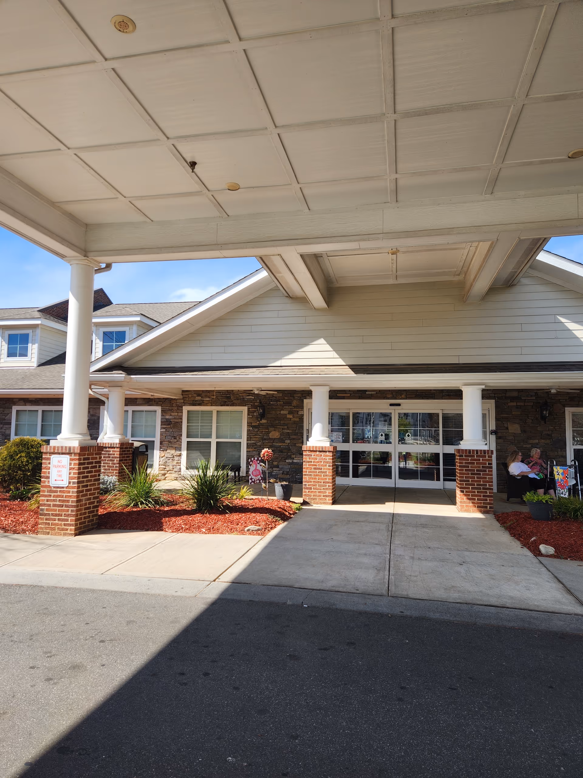 Entrance to a senior living facility with a covered drop-off, brick columns, and glass doors.