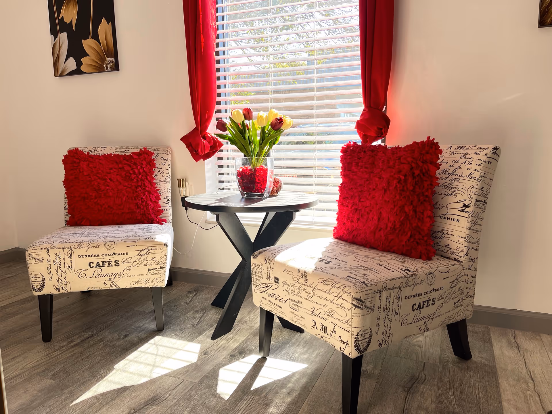 Cozy living room seating area with patterned chairs, red pillows, and a tulip bouquet.