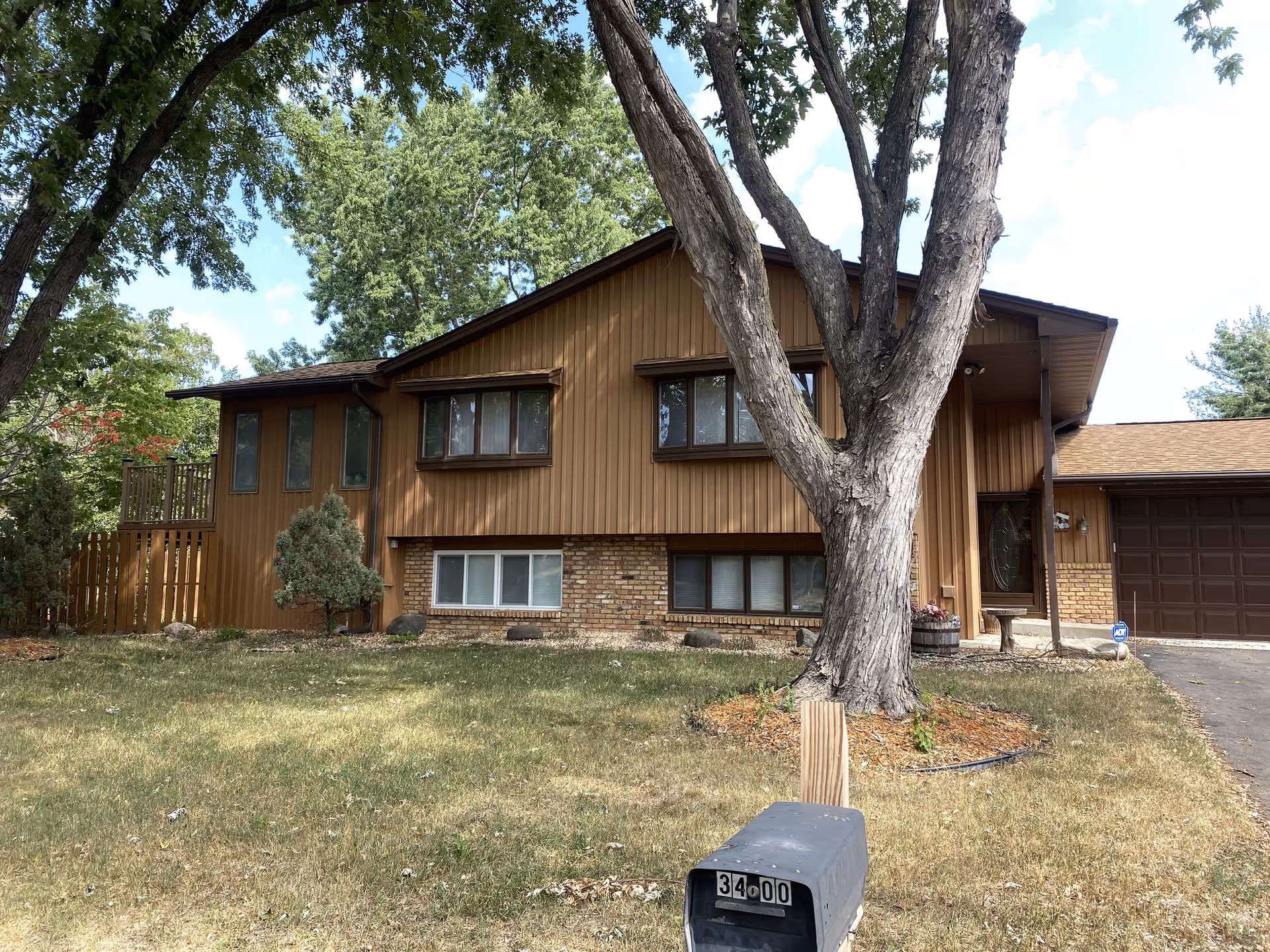 Brown wood-clad senior living facility front exterior with large tree, lawn, and driveway.