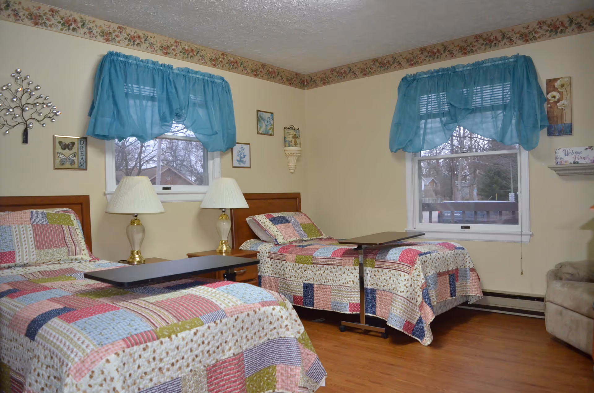 Two twin beds with patchwork quilts and blue curtains in a cozy resident bedroom.