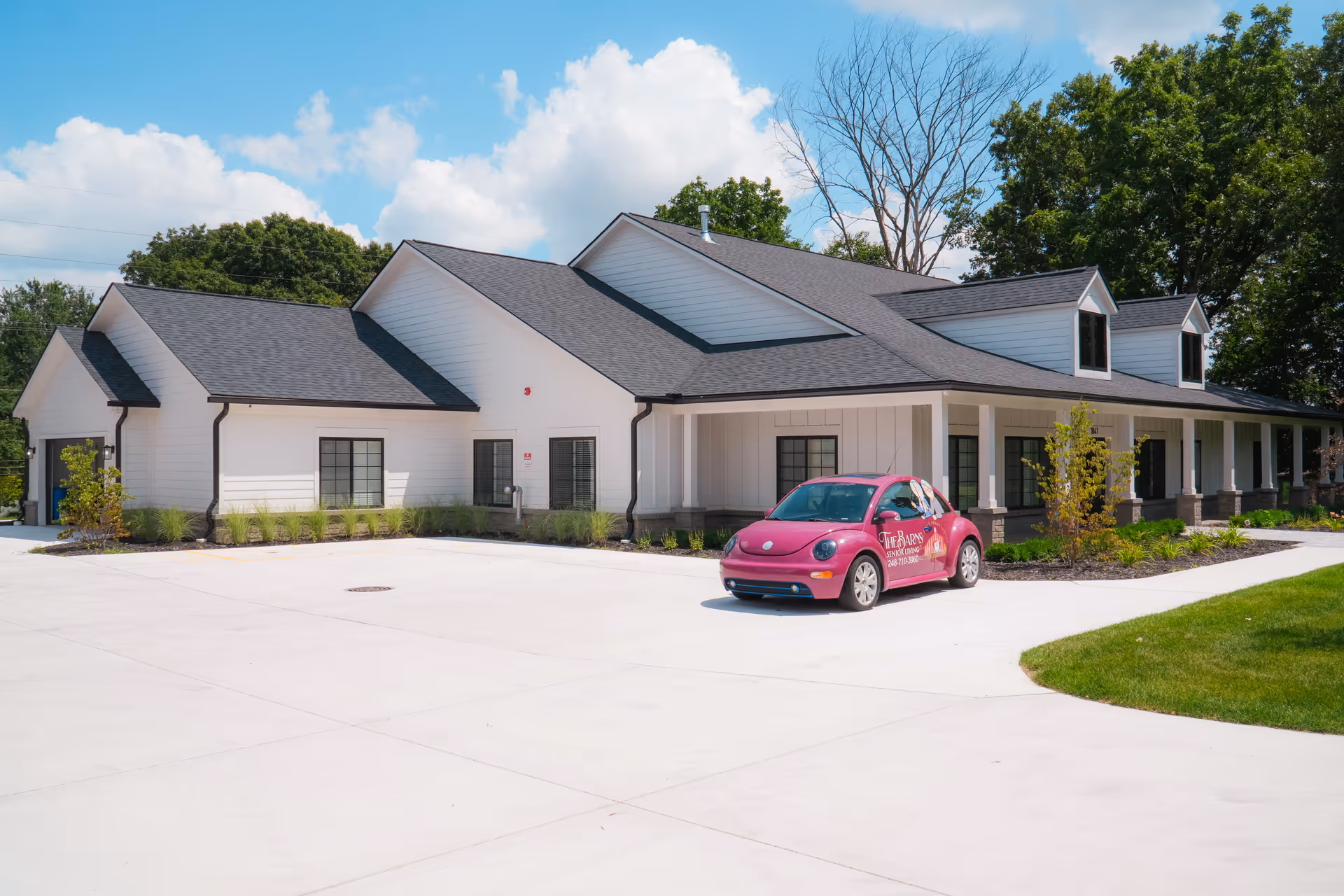 White modern senior living facility with dark roof and pink car parked front.