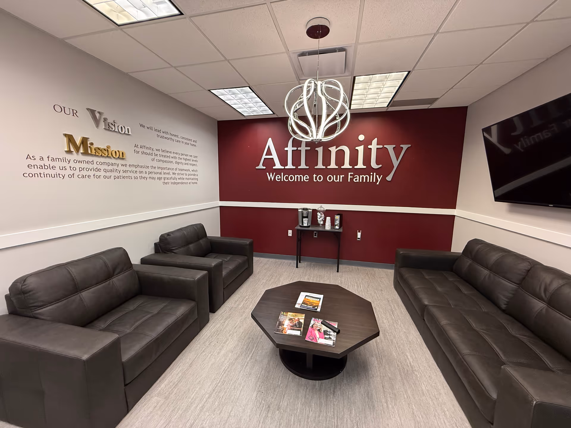 Waiting lounge with black leather sofas and burgundy accent wall under circular chandelier.