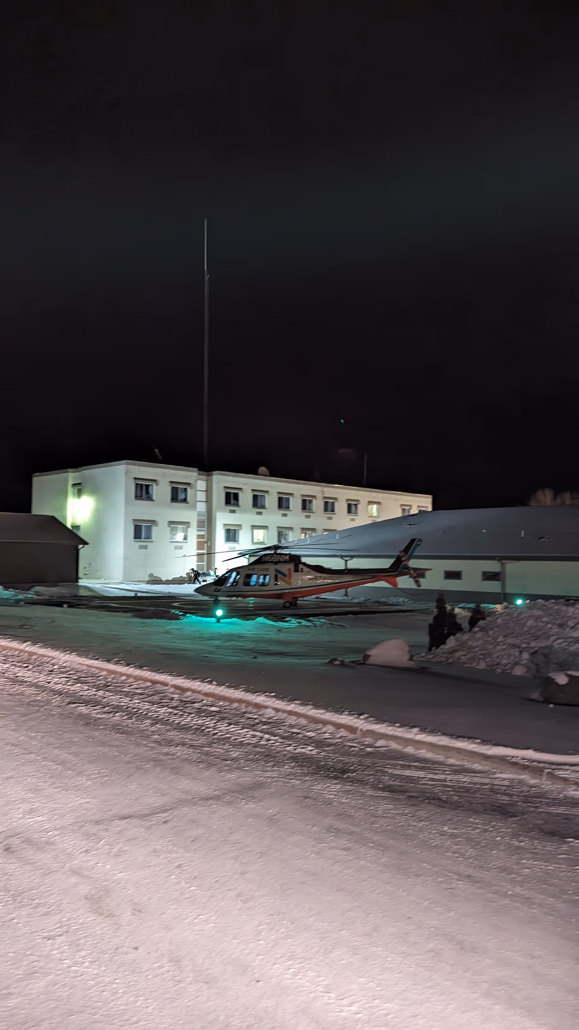 Night exterior of Indianhead Medical Center with a helicopter on snow in front.