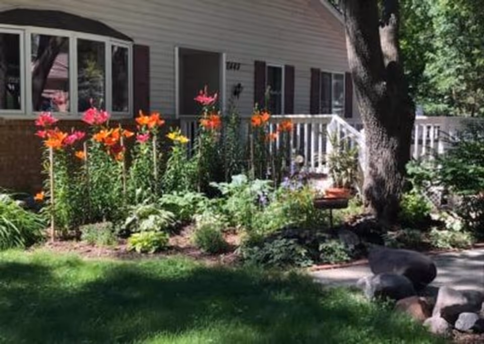 Exterior view of Hope's Residence with a flower garden, bushes, and large tree by the entrance.