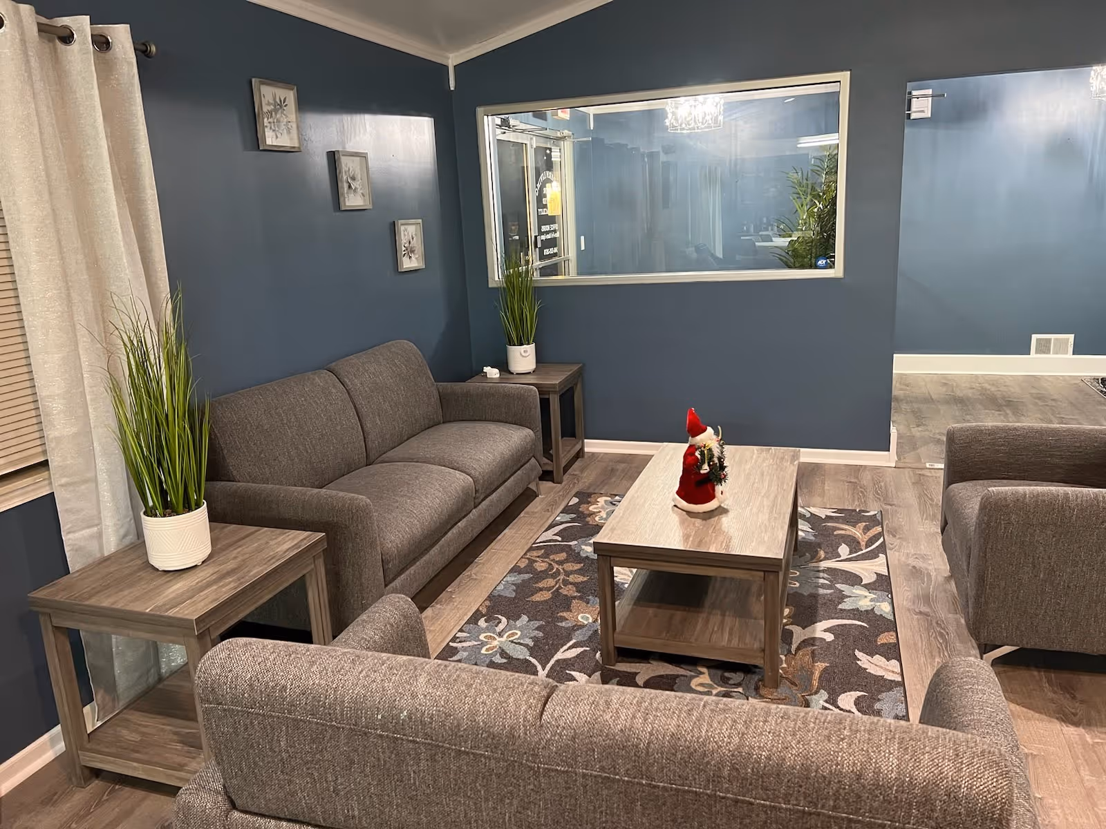 Cozy living room in a senior facility with gray couches, plants, and holiday decor.