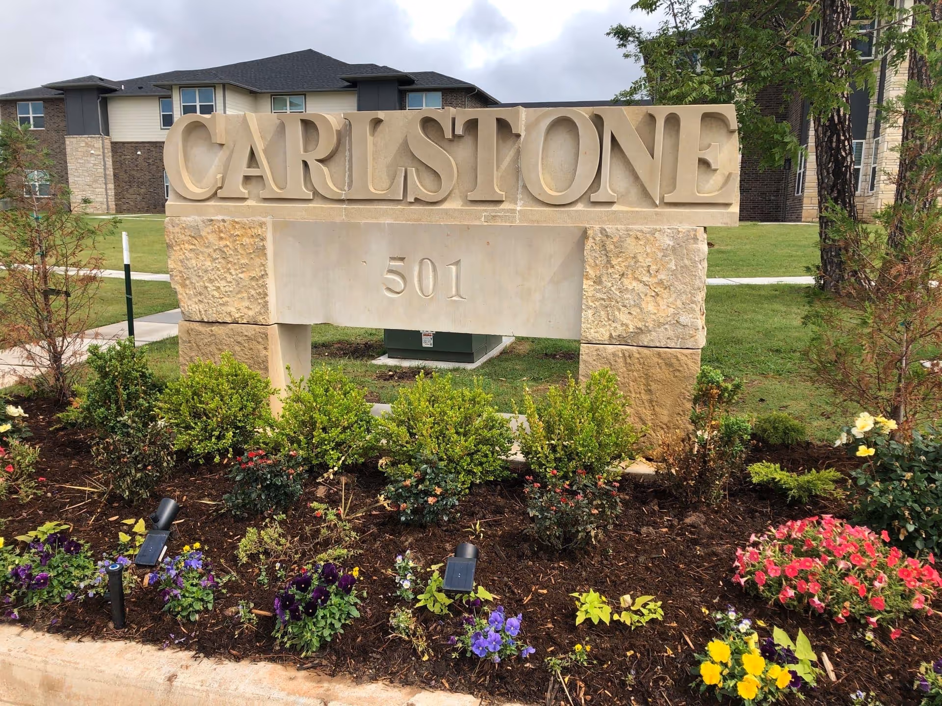 Carlstone sign with landscaped garden and a residential building in the background.