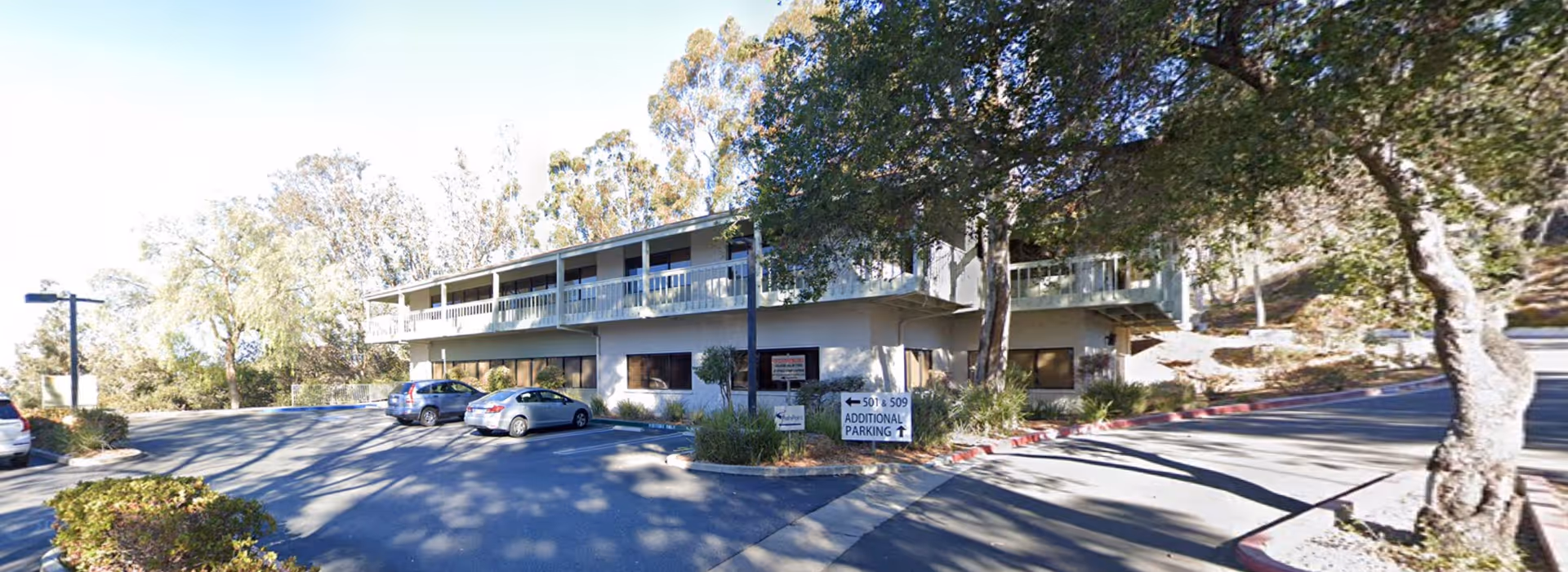 Exterior view of a two-story senior care building with parking and surrounding trees.