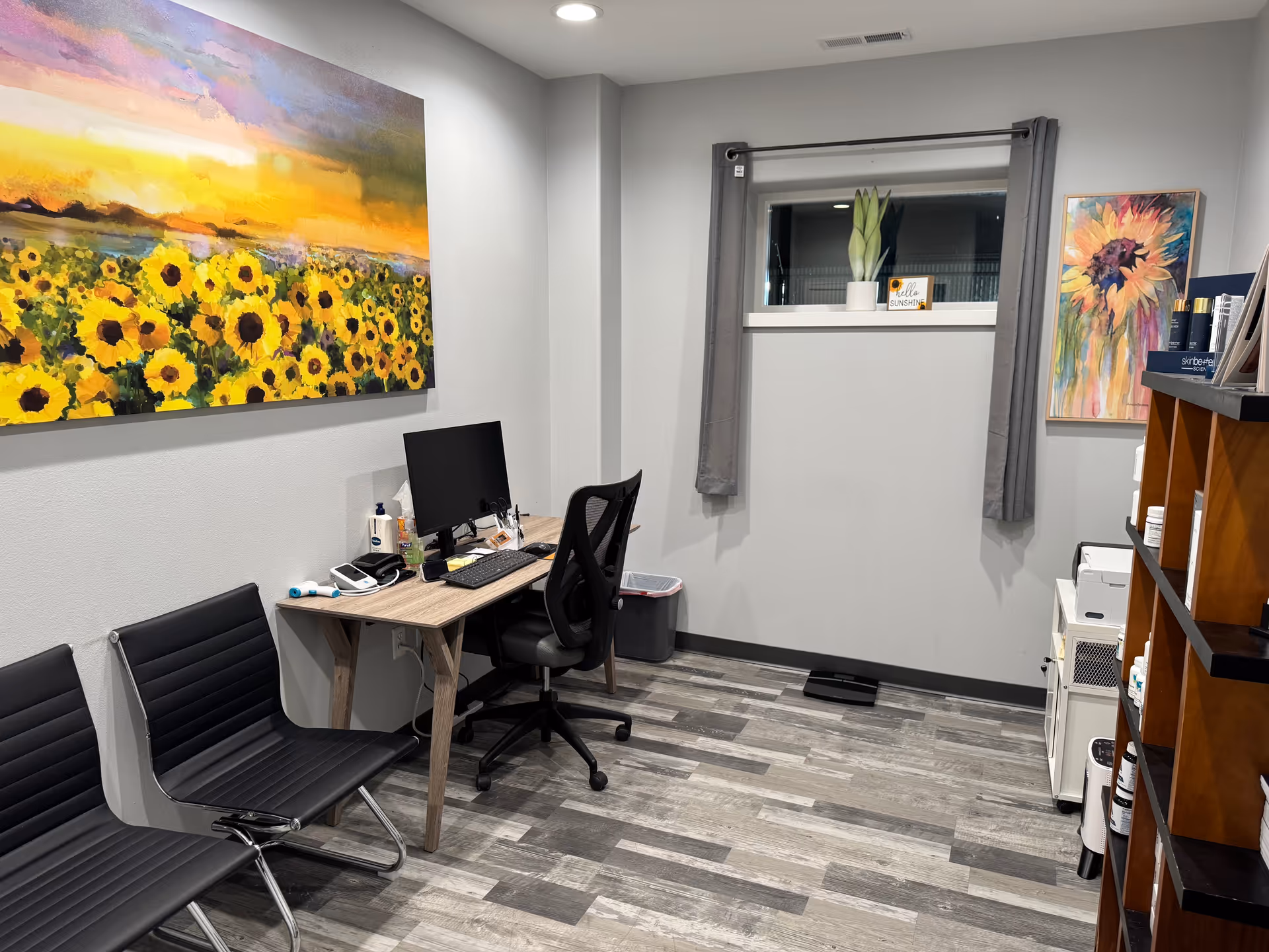 Small office with desk, computer, two chairs, window, and colorful wall art.