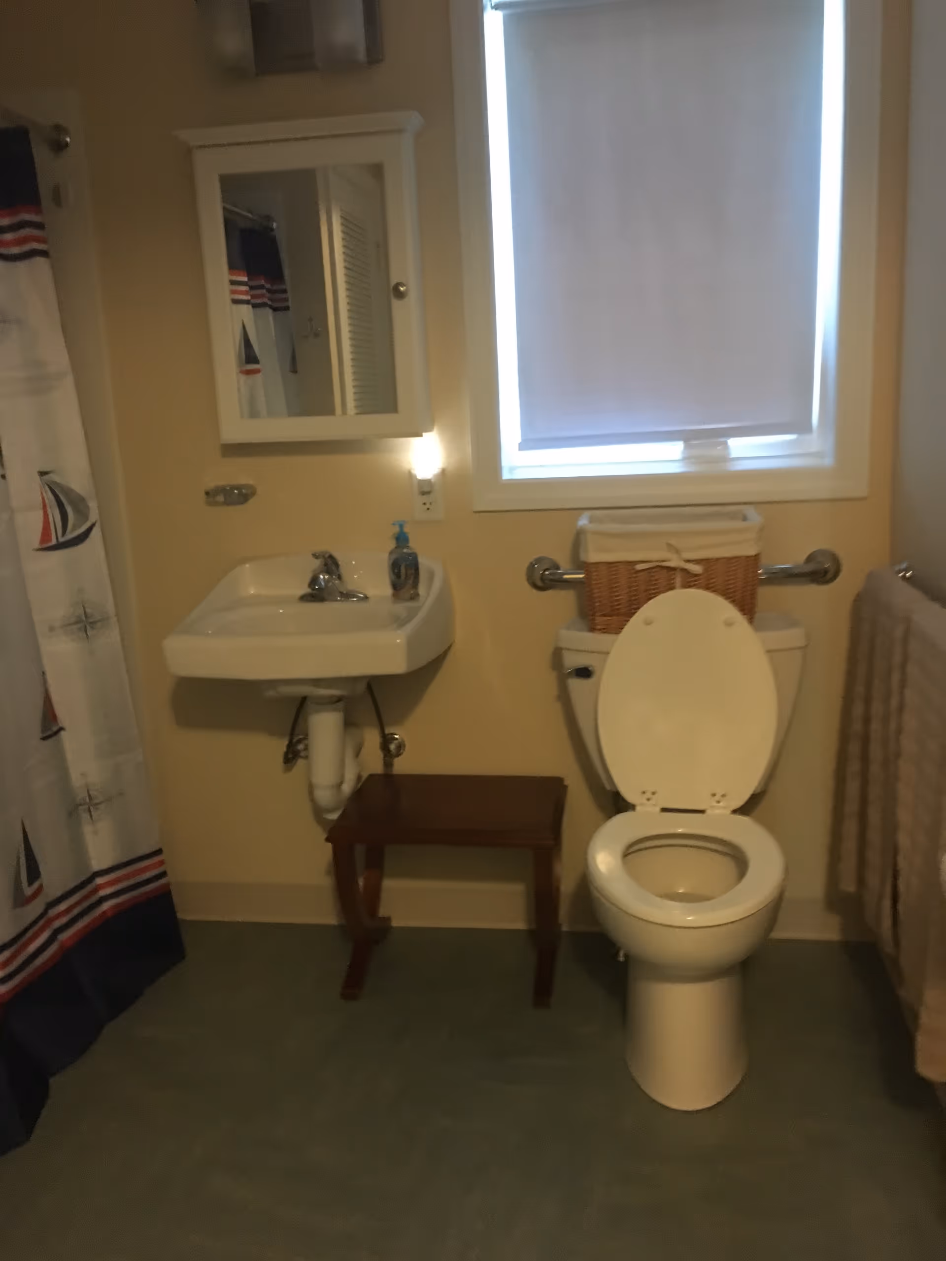 Small bathroom with sink, toilet, mirror cabinet, window, and a nautical shower curtain.