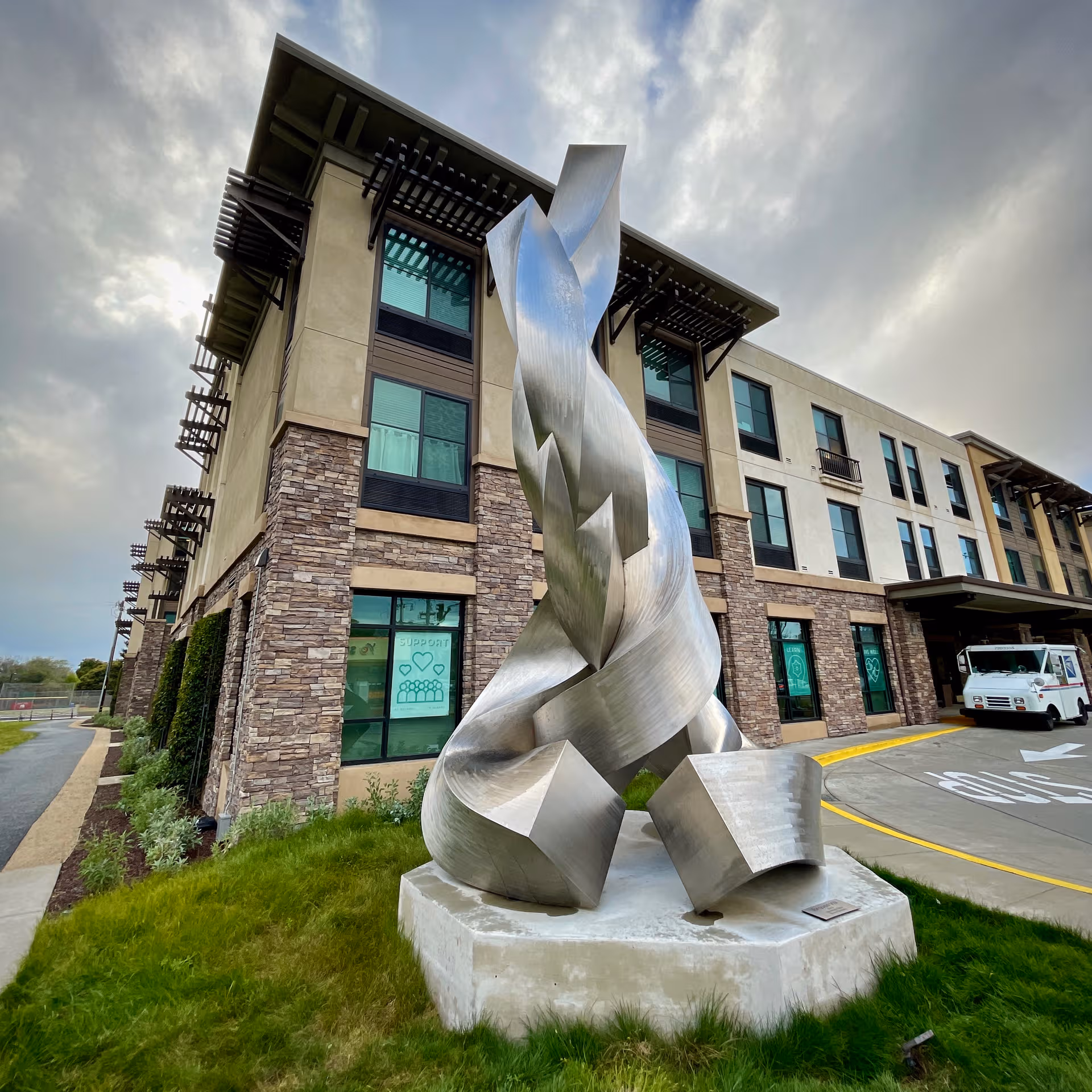 Modern multi-story senior living building featuring a tall metallic abstract sculpture at the front entrance.