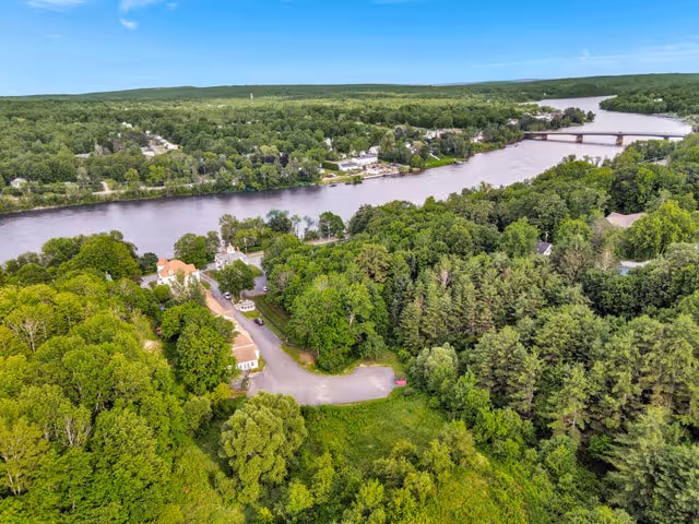 Aerial view of wooded grounds, river, and a bridge near residential houses.