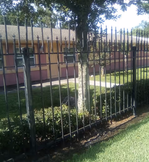 Metal fence in foreground with a pinkish exterior facility and green lawn beyond.