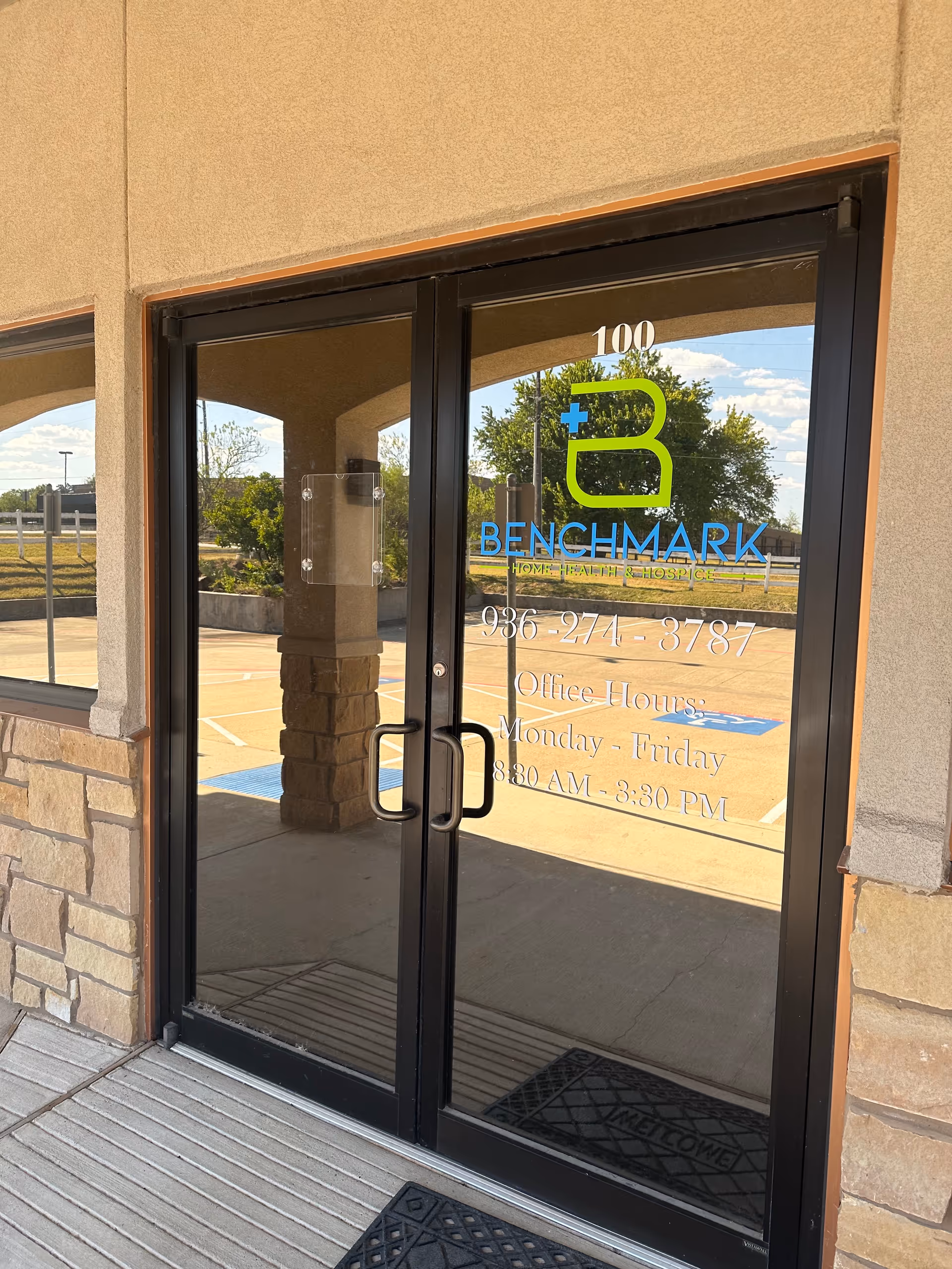 Glass double doors with Benchmark logo and office hours at a beige building entrance.