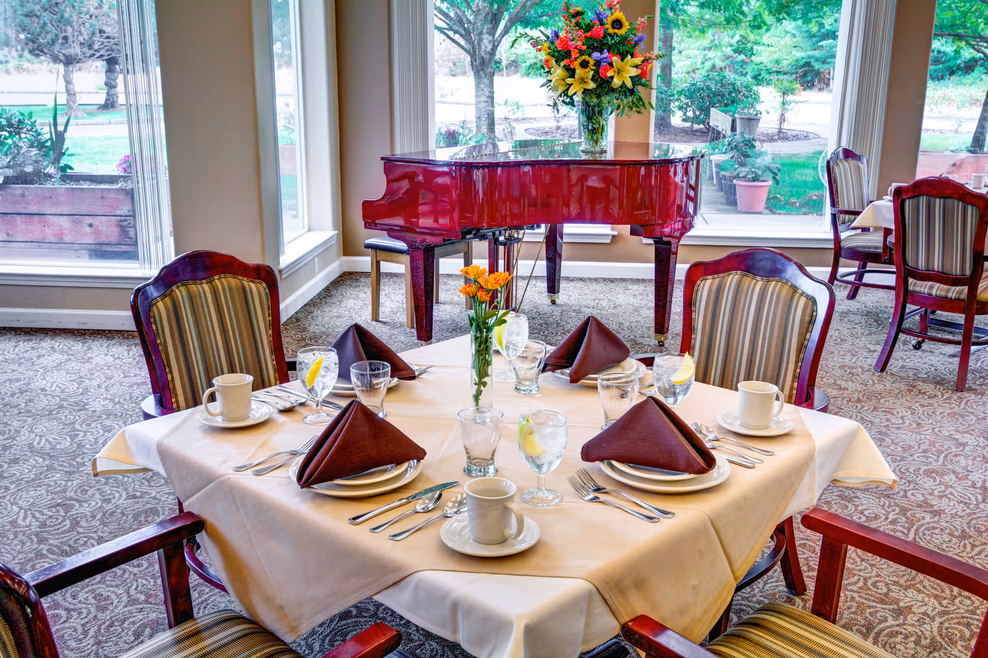 Elegant dining room with a red piano, round table, and floral centerpiece.