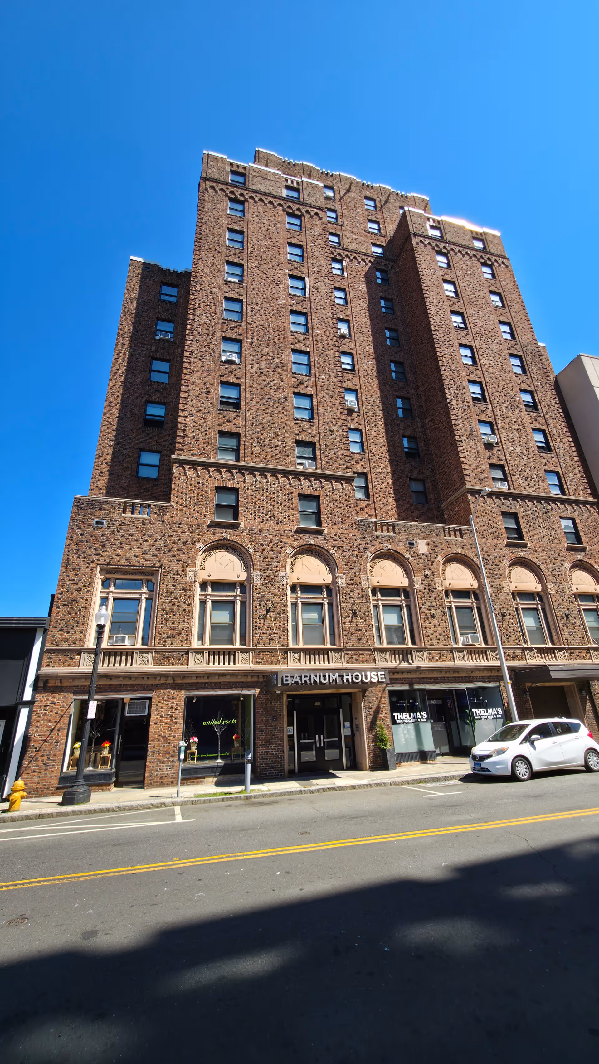 Tall brick building with arched windows and Barnum House sign on storefront, blue sky.