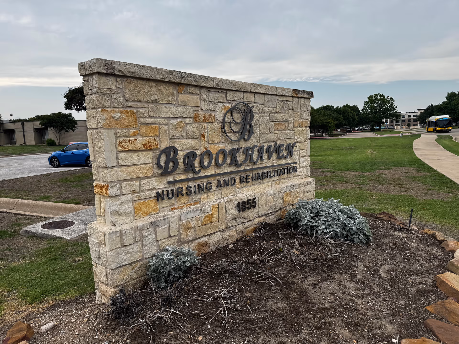 Stone Brookhaven Nursing and Rehabilitation sign with landscaping and a distant road.
