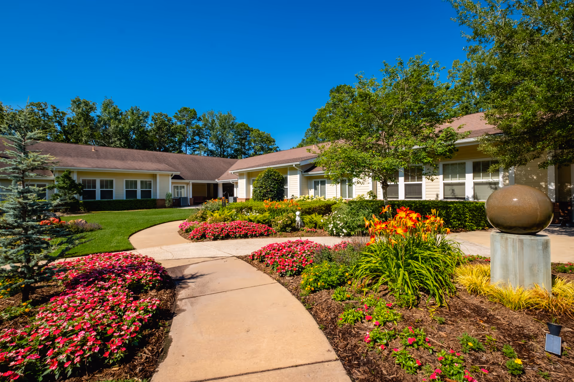 Senior living facility with a landscaped entrance, colorful flowerbeds, and a curved walkway.