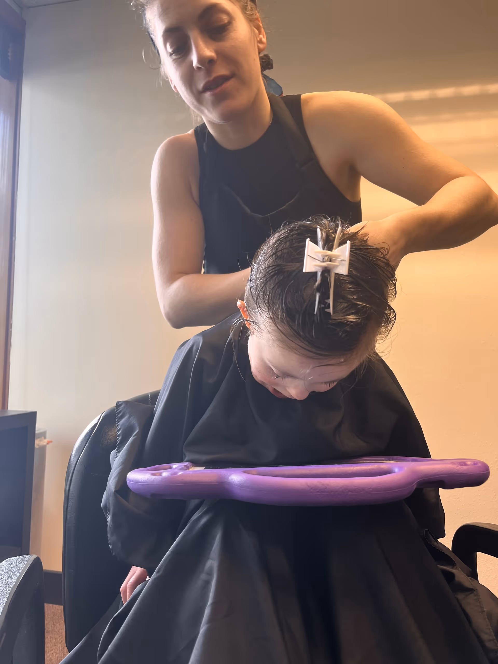 Hairdresser trims a client's hair in a salon with a purple cape.