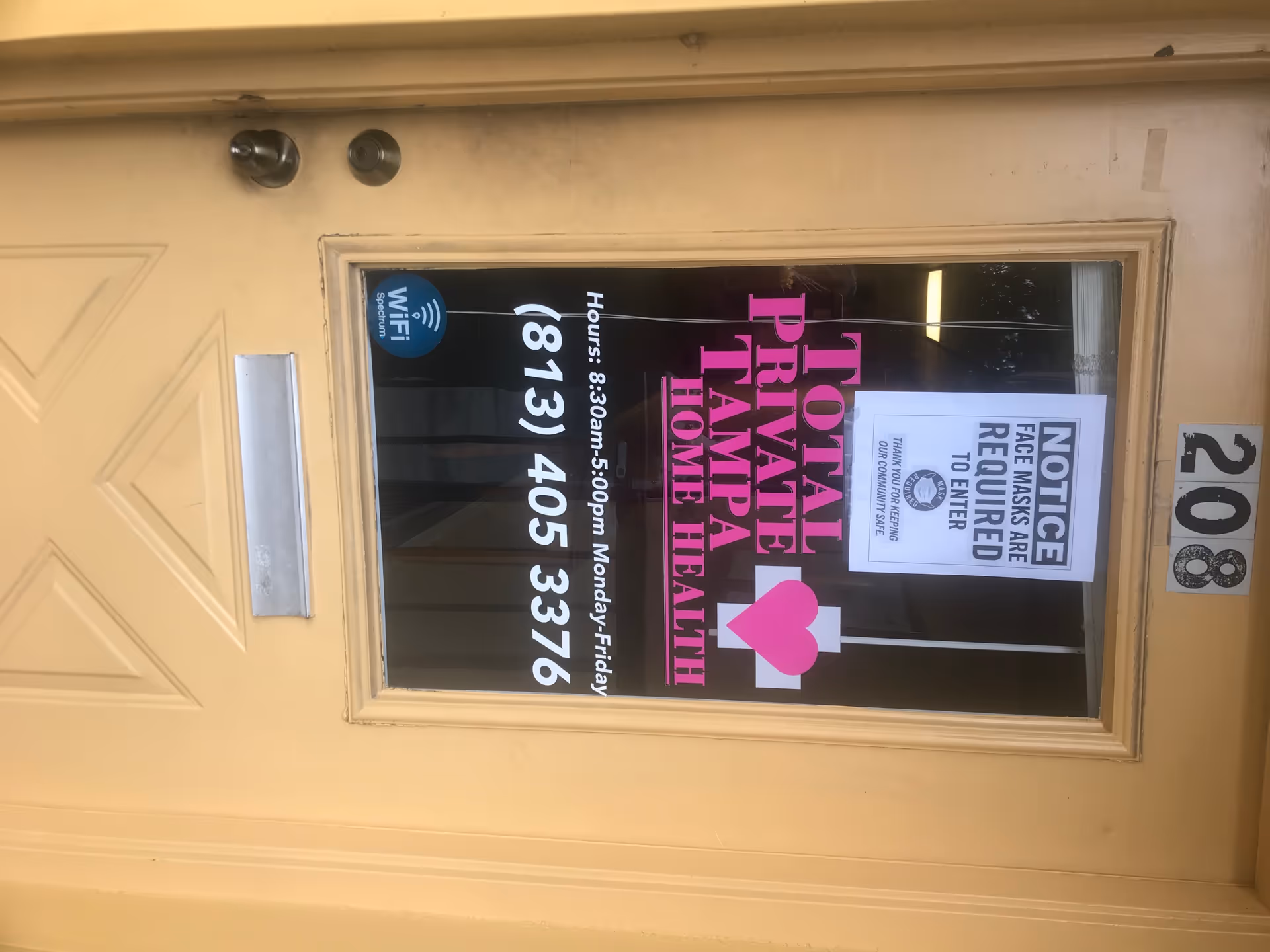 Beige entry door displays pink Total Private Tampa Home Health sign and various notices.