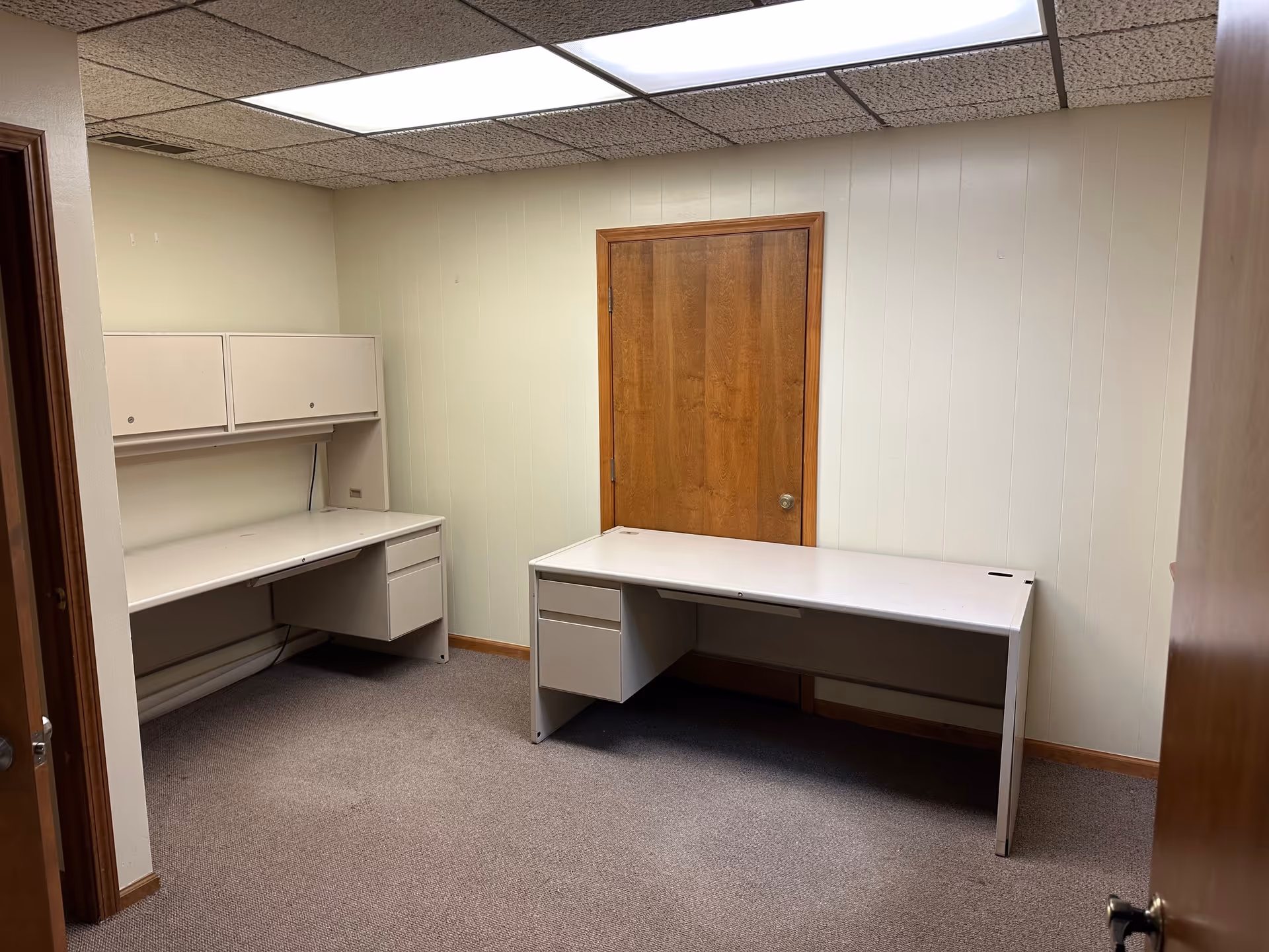 Empty office space with desks, cabinets, and a wooden door.