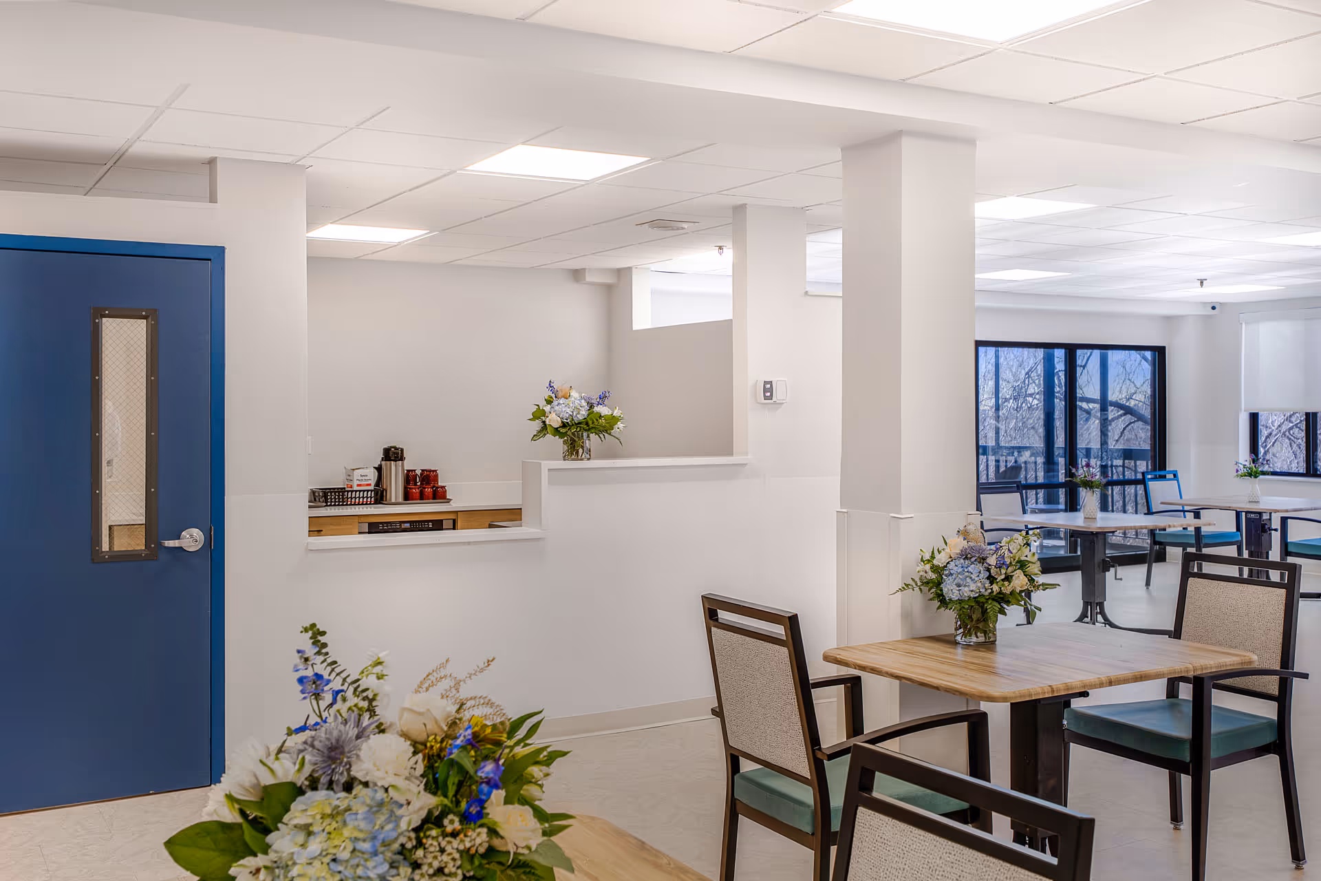 A bright, modern dining area with tables, chairs, and floral decor in a senior facility.
