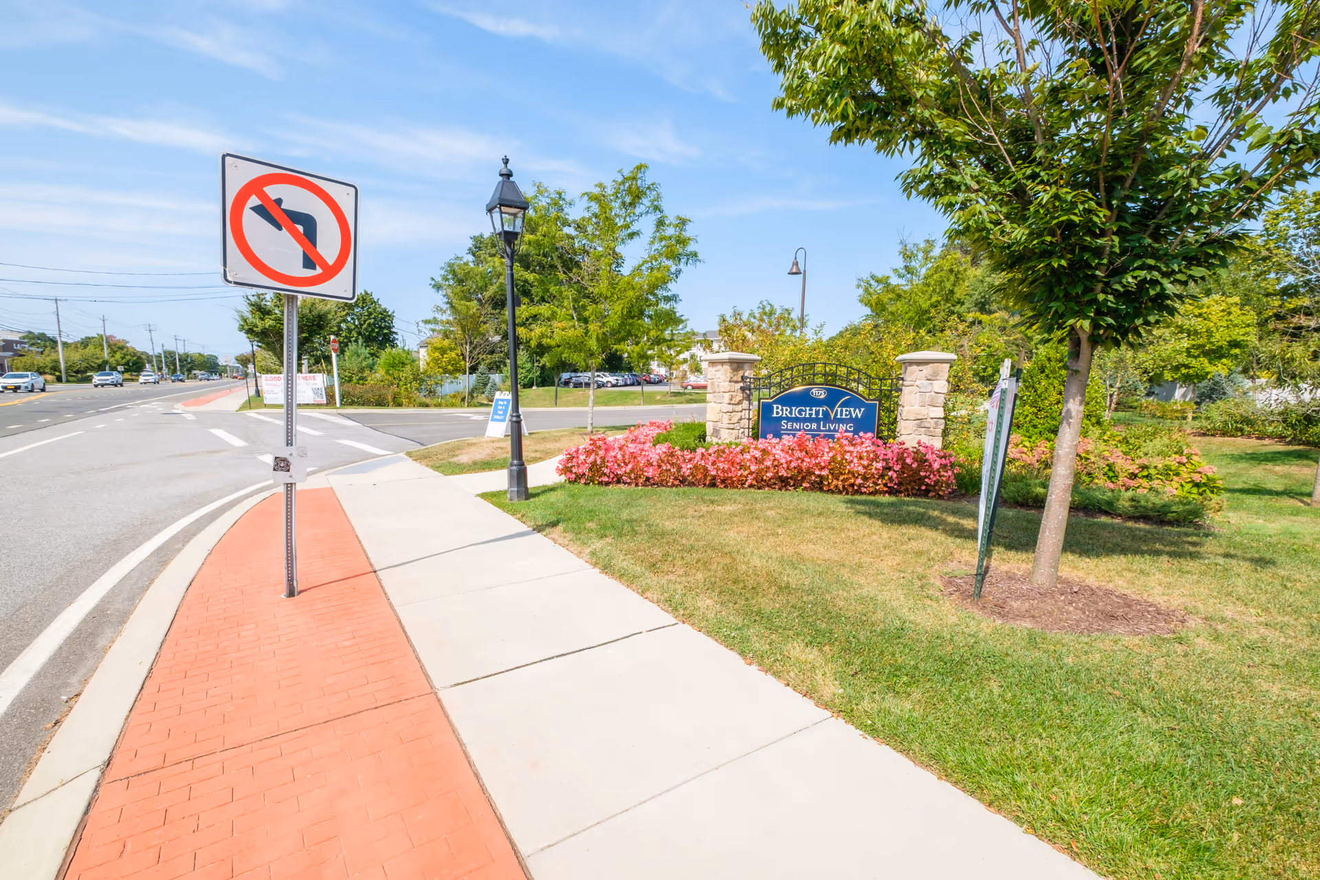 Sidewalk and landscaped entrance with a sign for Bright View Senior Living beside a road and a no-left-turn sign.
