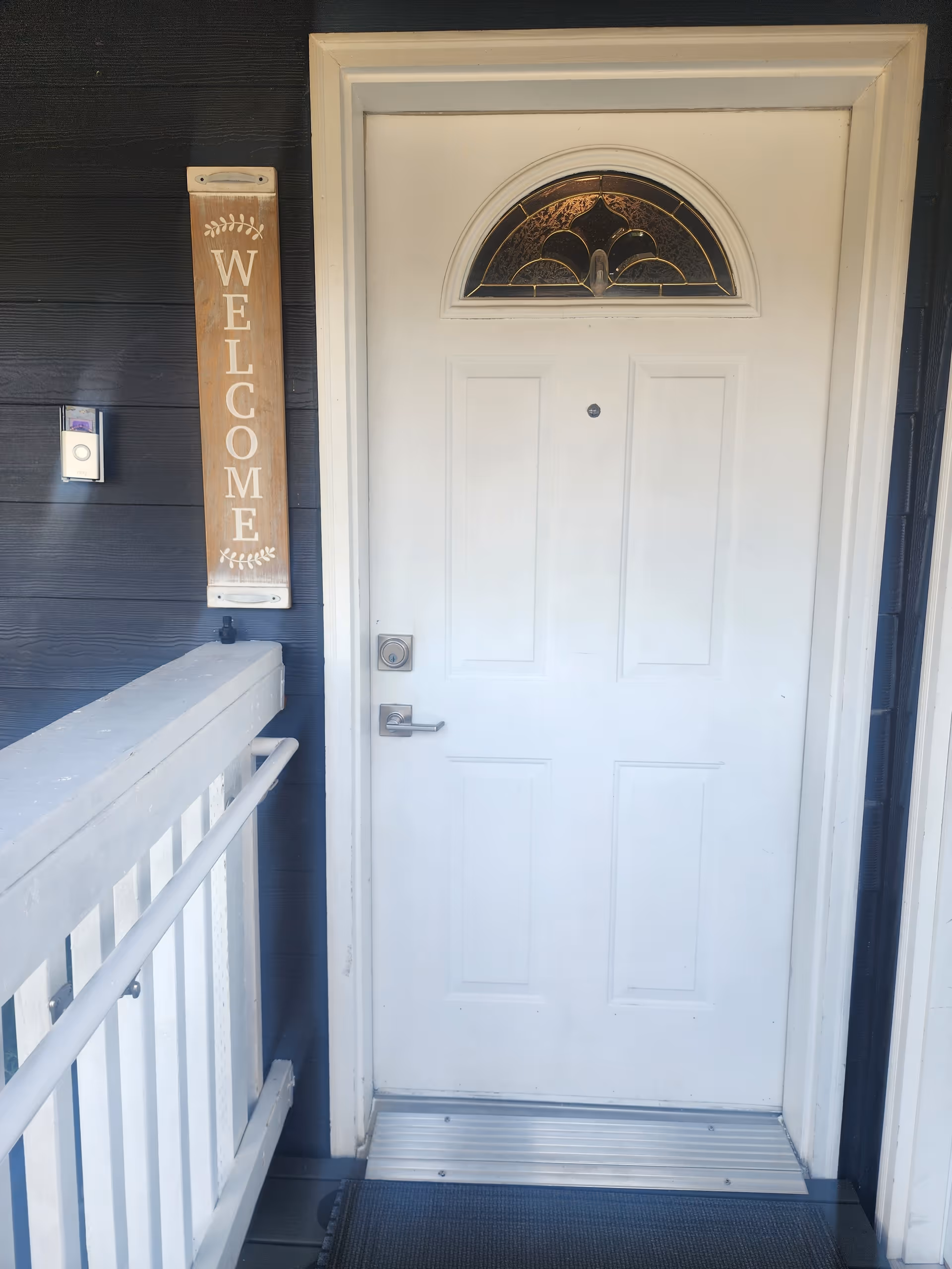 White front door with arched window and welcome sign on dark exterior wall