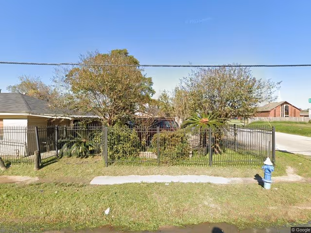 Front view of a single-story building behind a metal fence with trees and a fire hydrant on the grassy verge.