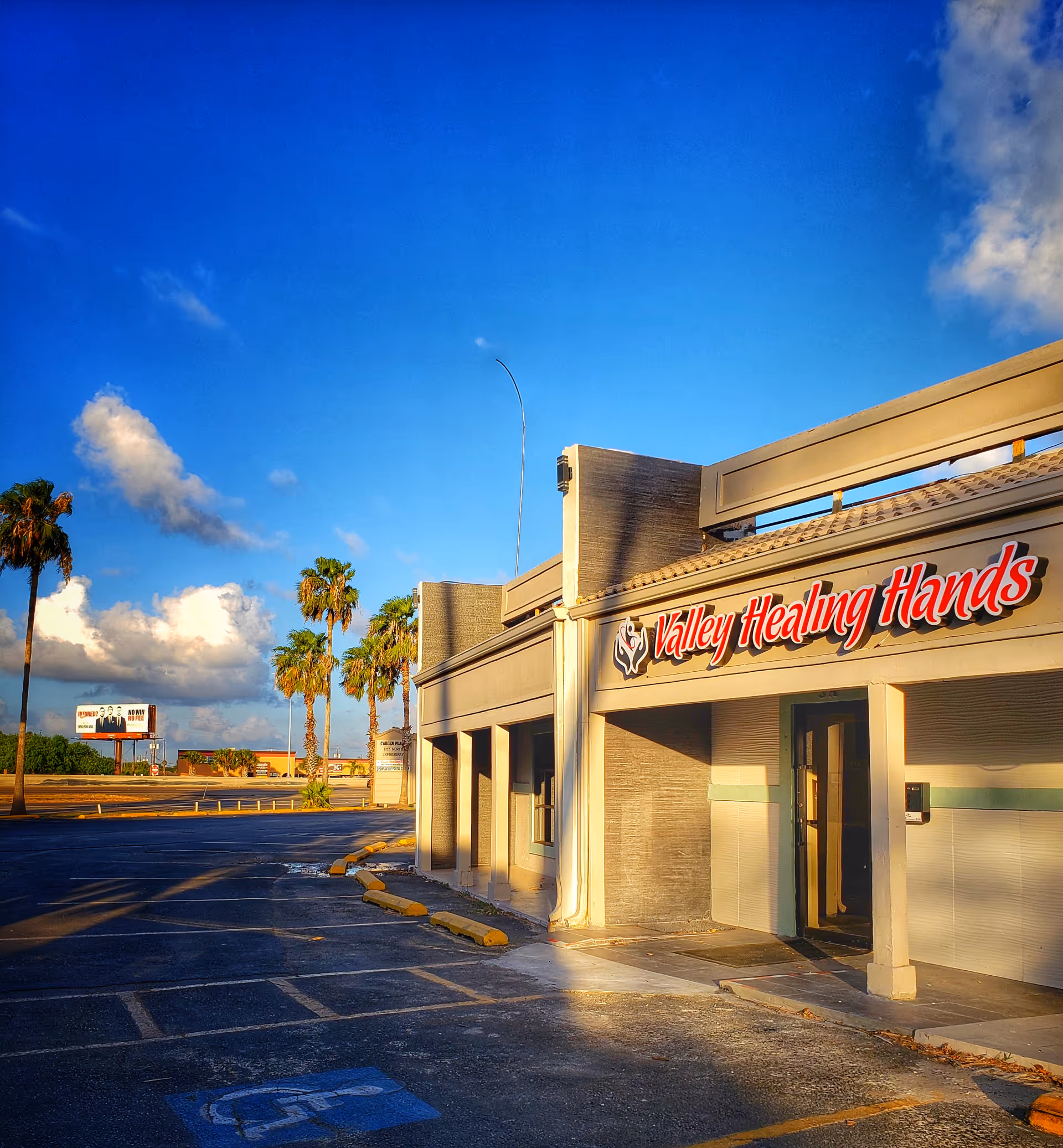 Exterior view of a Valley Healing Hands facility with palm trees and a clear blue sky.