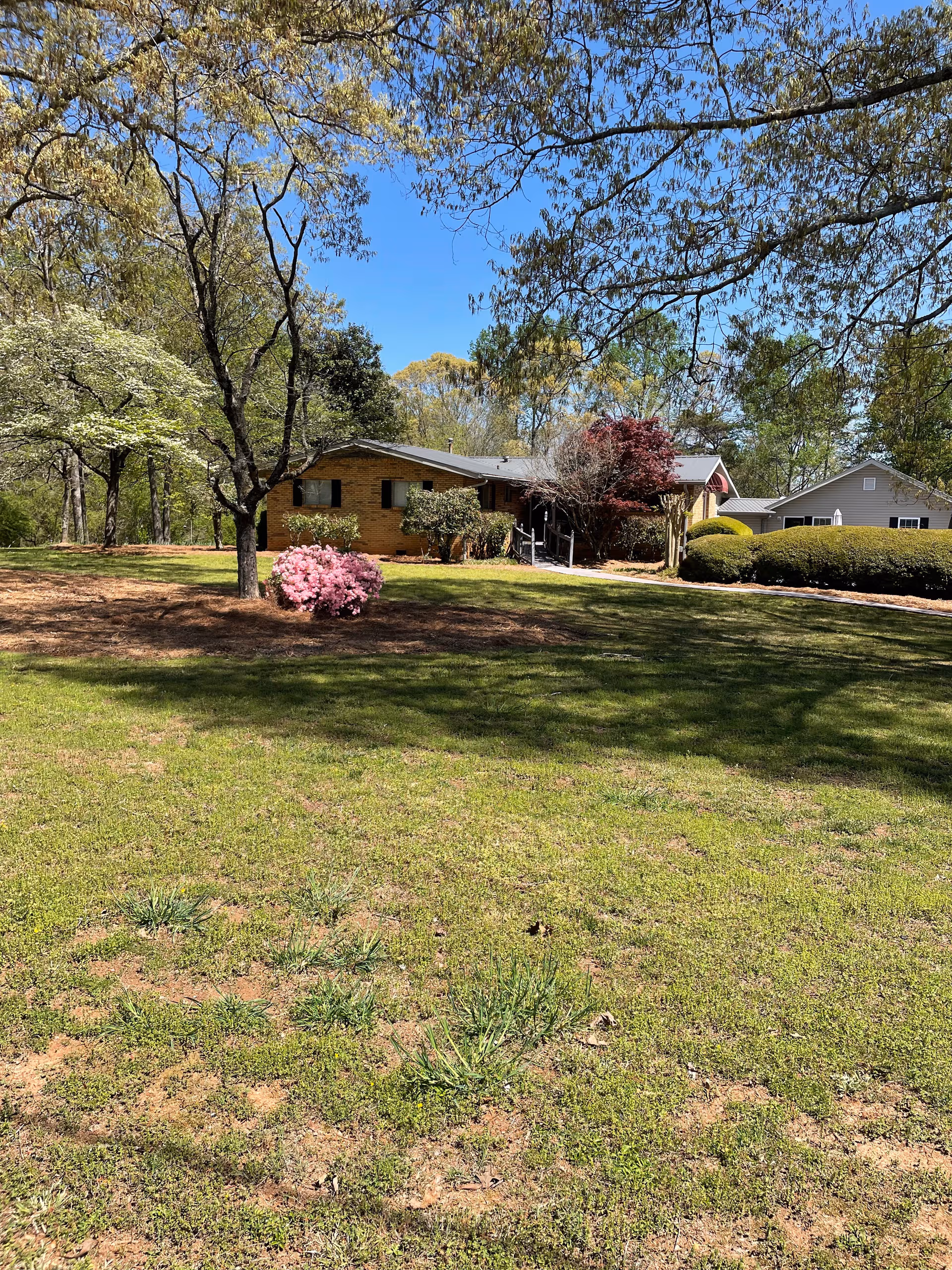 Exterior view of a single-story brick building with a green lawn, trees, and bushes.