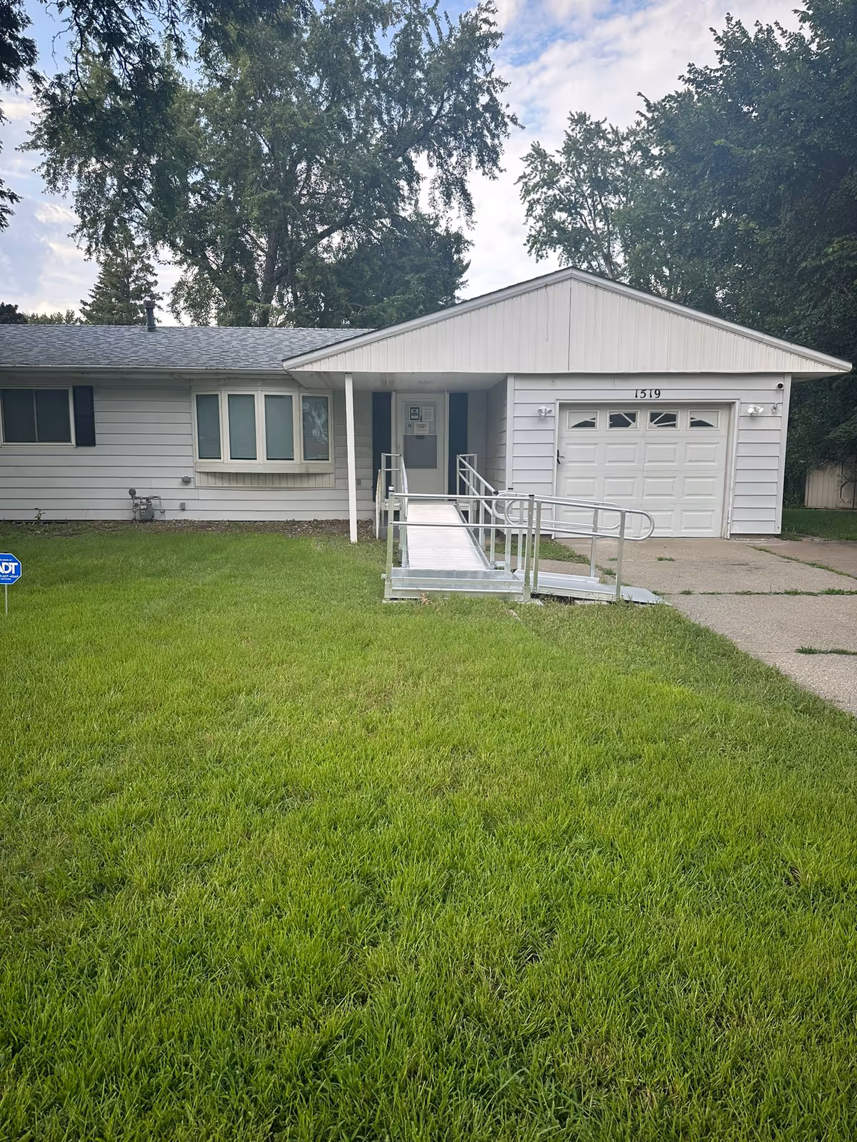 Single-story house exterior with ramped entry and attached garage by a green lawn.