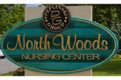 Oval teal sign reads North Woods Nursing Center with gold lettering, surrounded by greenery.