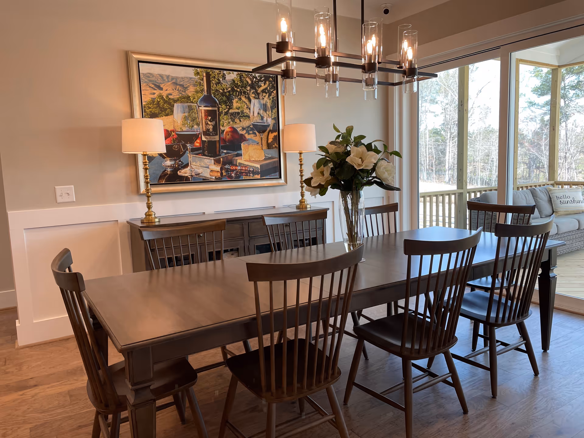 A dining room with a long wooden table, chairs, chandelier, and sliding glass doors.