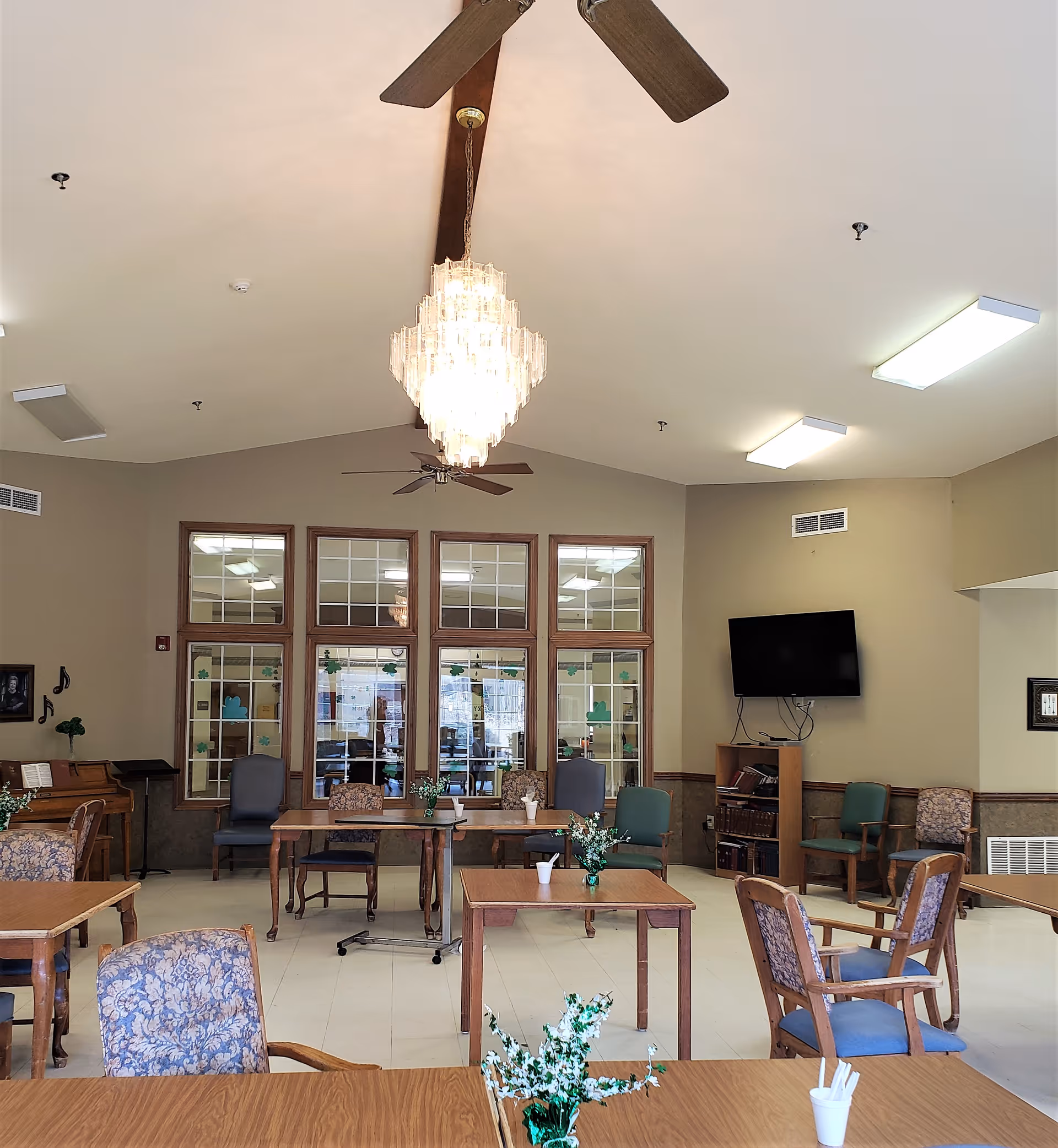 Spacious indoor common area with tables, chairs, a chandelier, and ceiling fans.