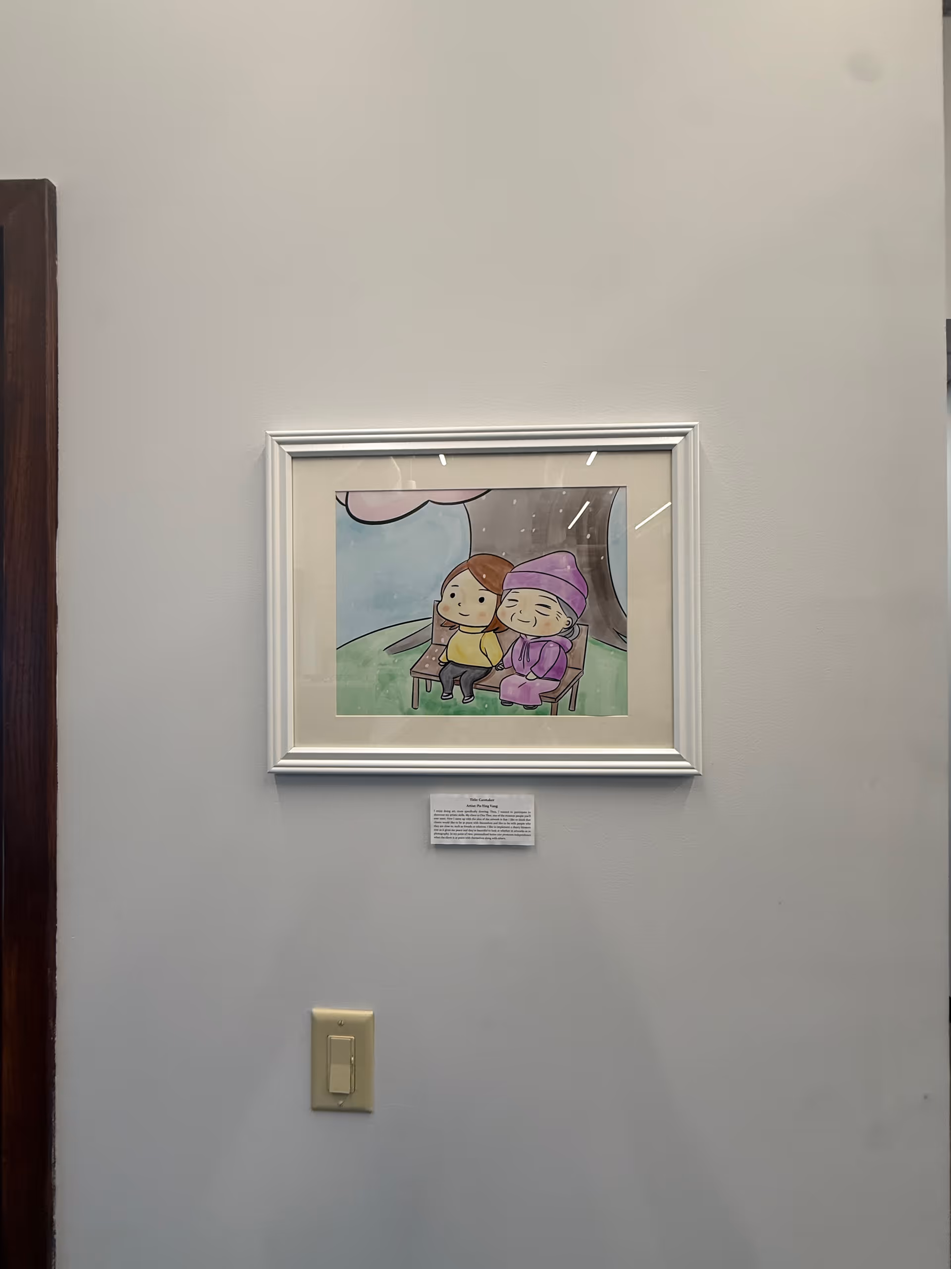 Framed cartoon artwork hangs on a white wall above a beige light switch.
