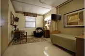 A small senior living bedroom with a bed, chair, dresser, and window.