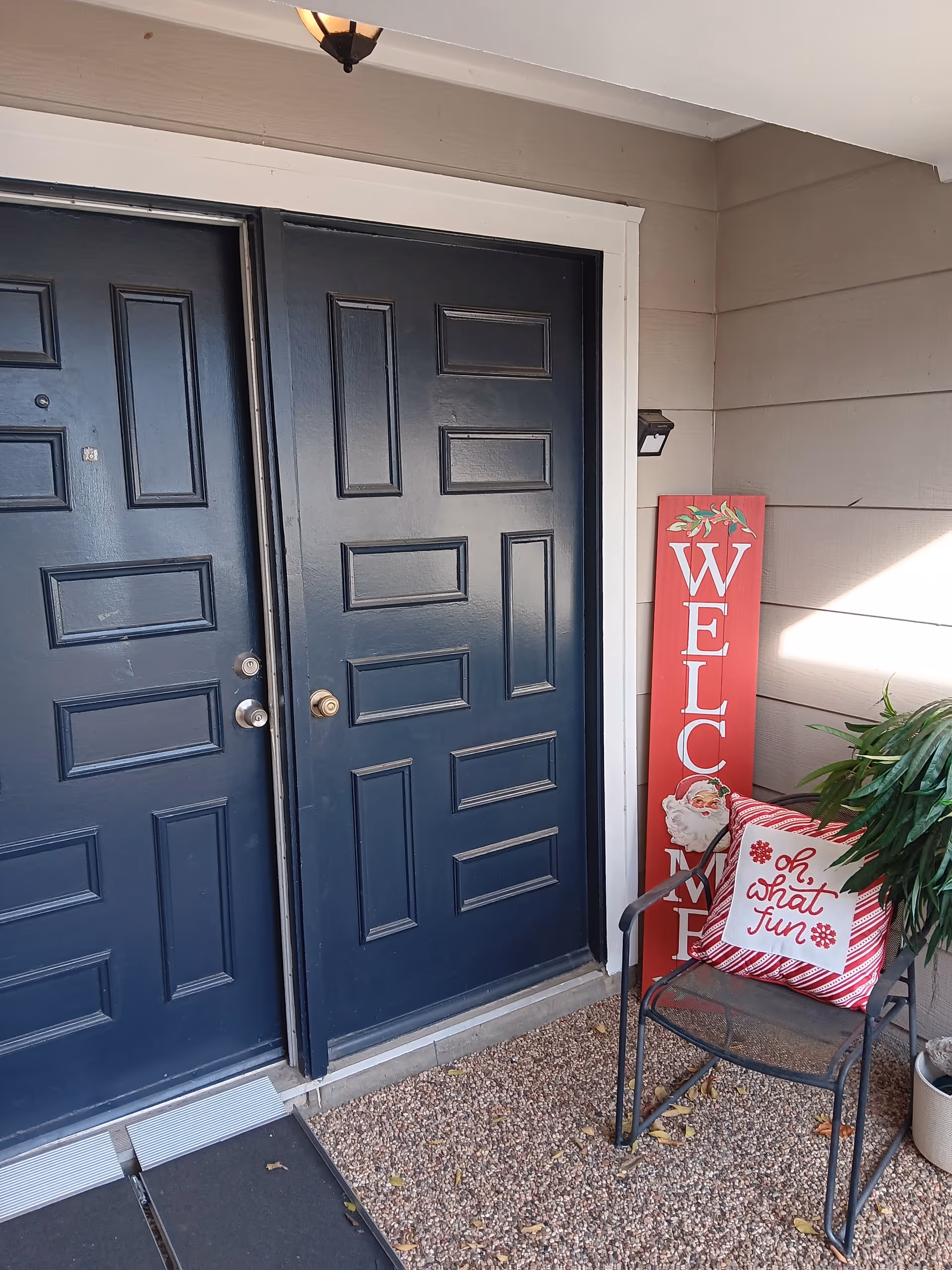 Two dark blue front doors with a welcome sign and a chair on the porch.