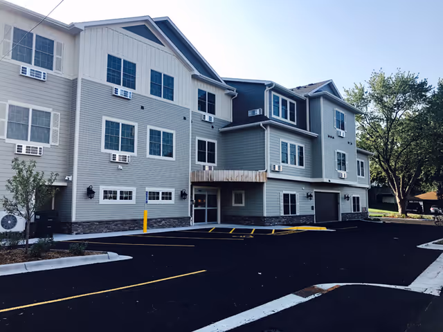 Exterior view of a multi-story senior living building with parking and trees.
