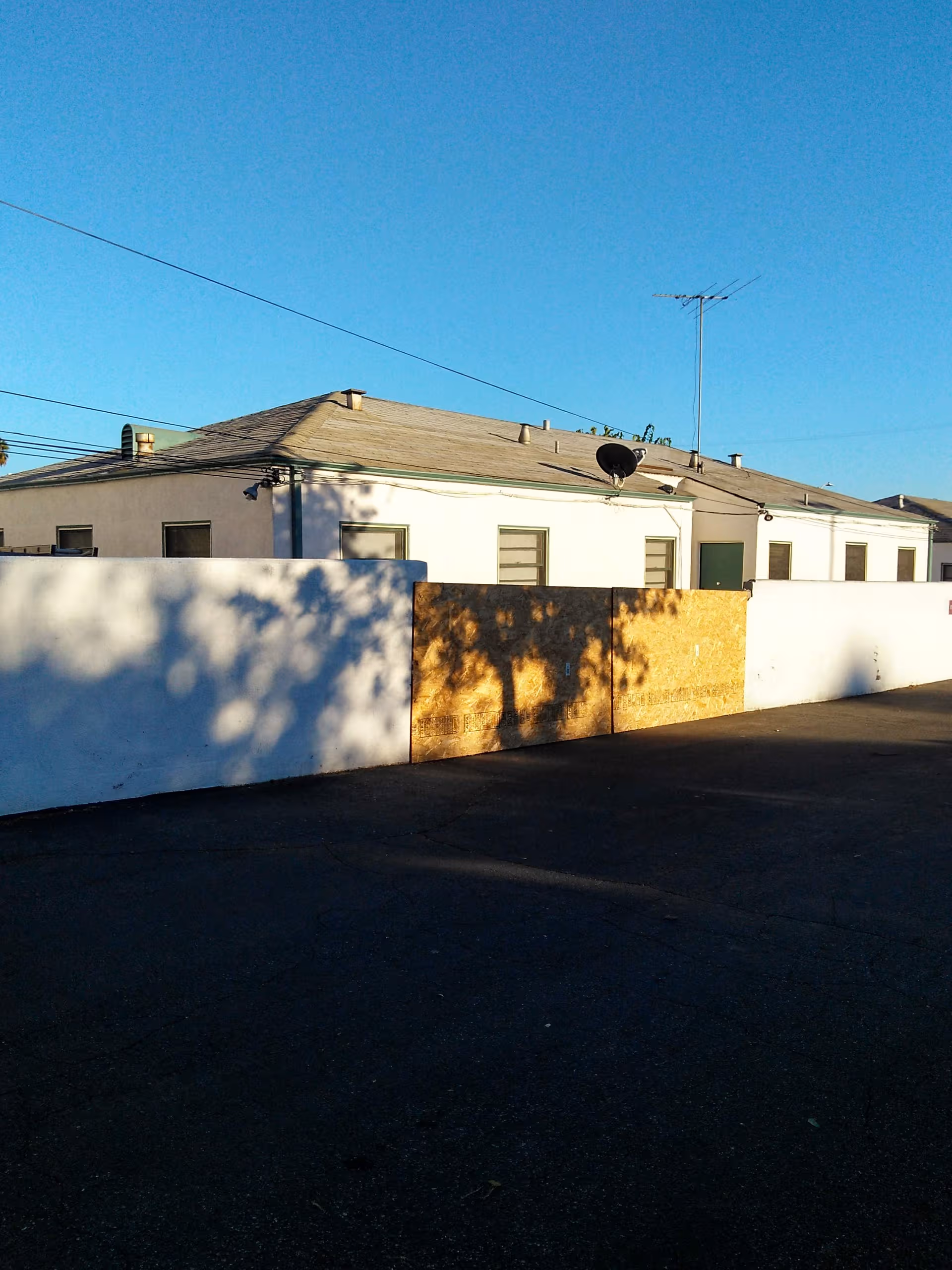White building with a tall wooden gate along a paved road under a clear blue sky.