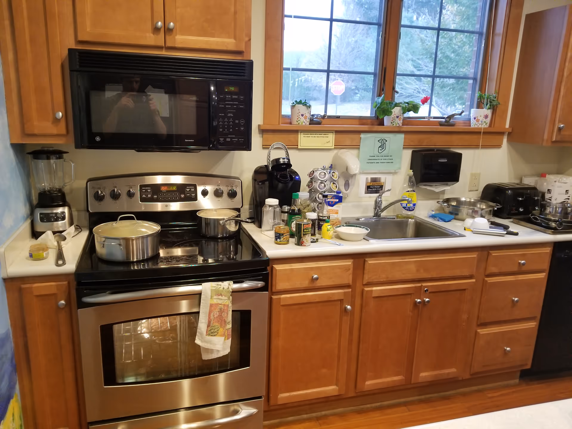 Kitchen with stove, microwave, sink, and wooden cabinets in a hospice facility.